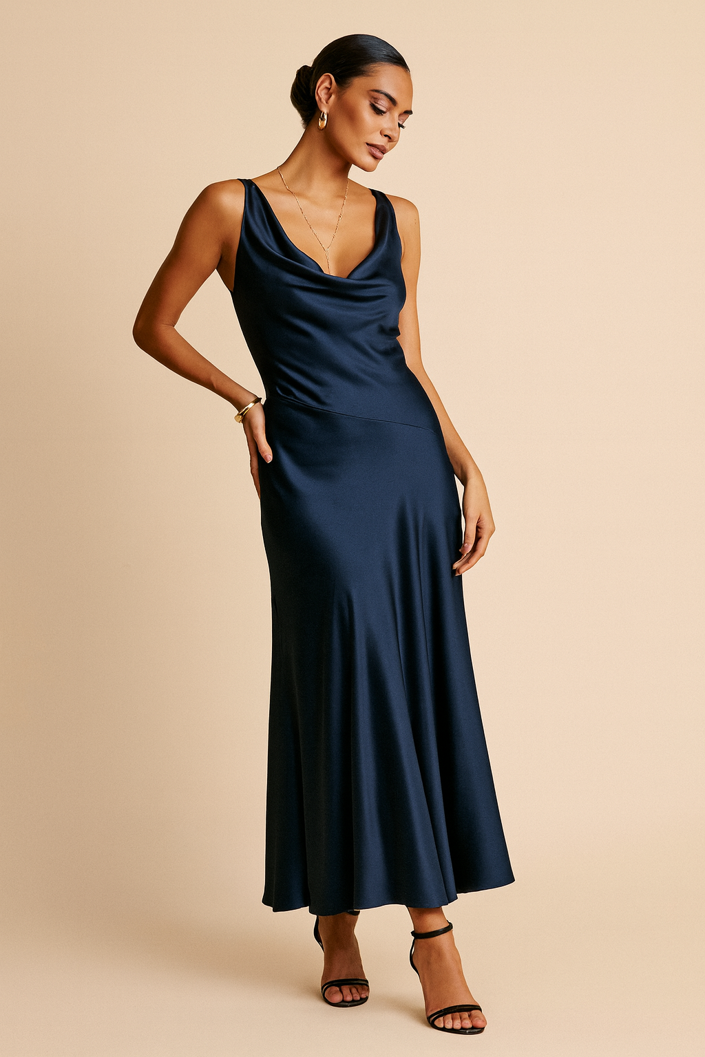 Woman wearing a navy satin maxi dress with a draped cowl neck, low open back tied at the shoulders, and a flared hem.