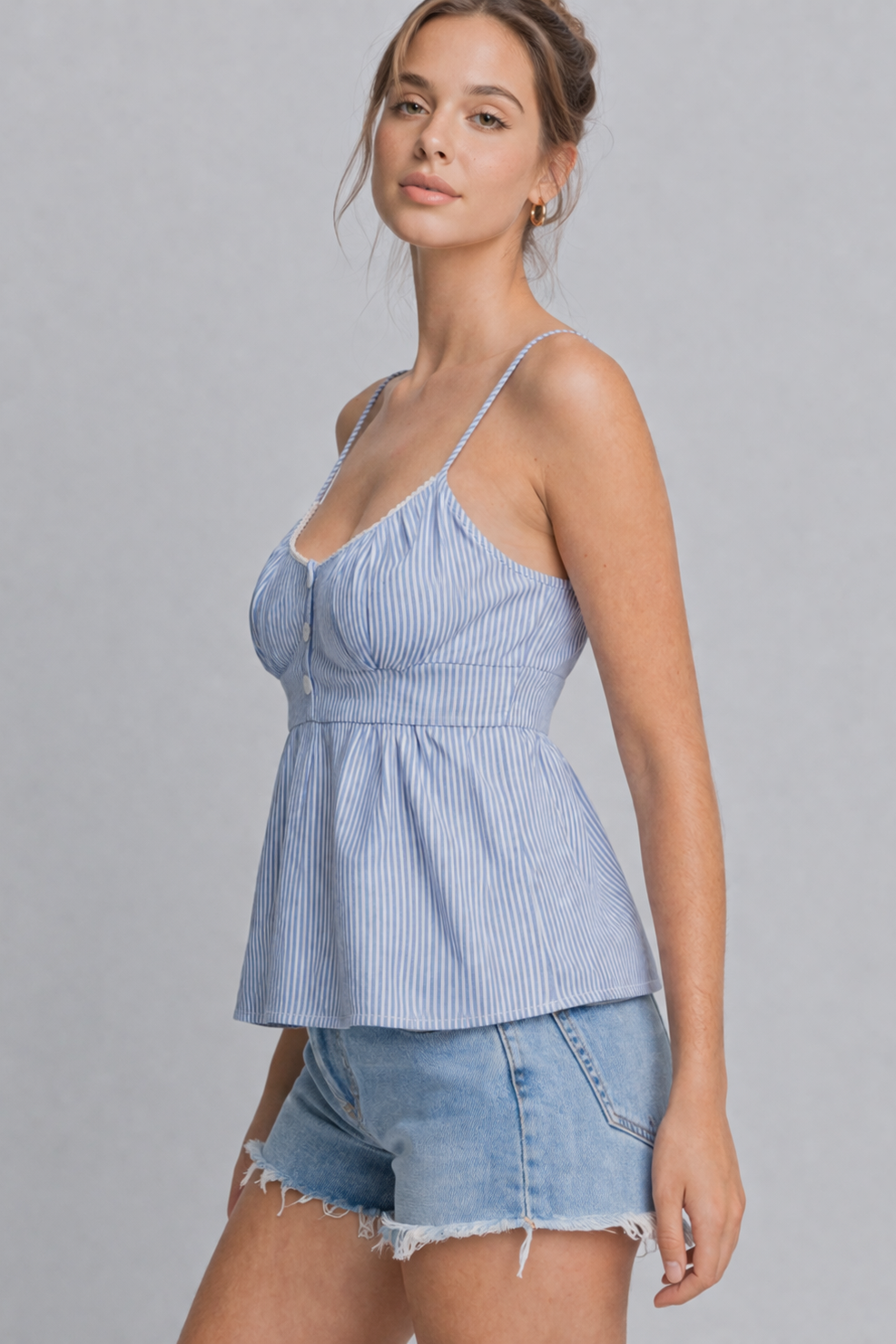 Woman wearing a blue striped top and denim shorts on a gray background