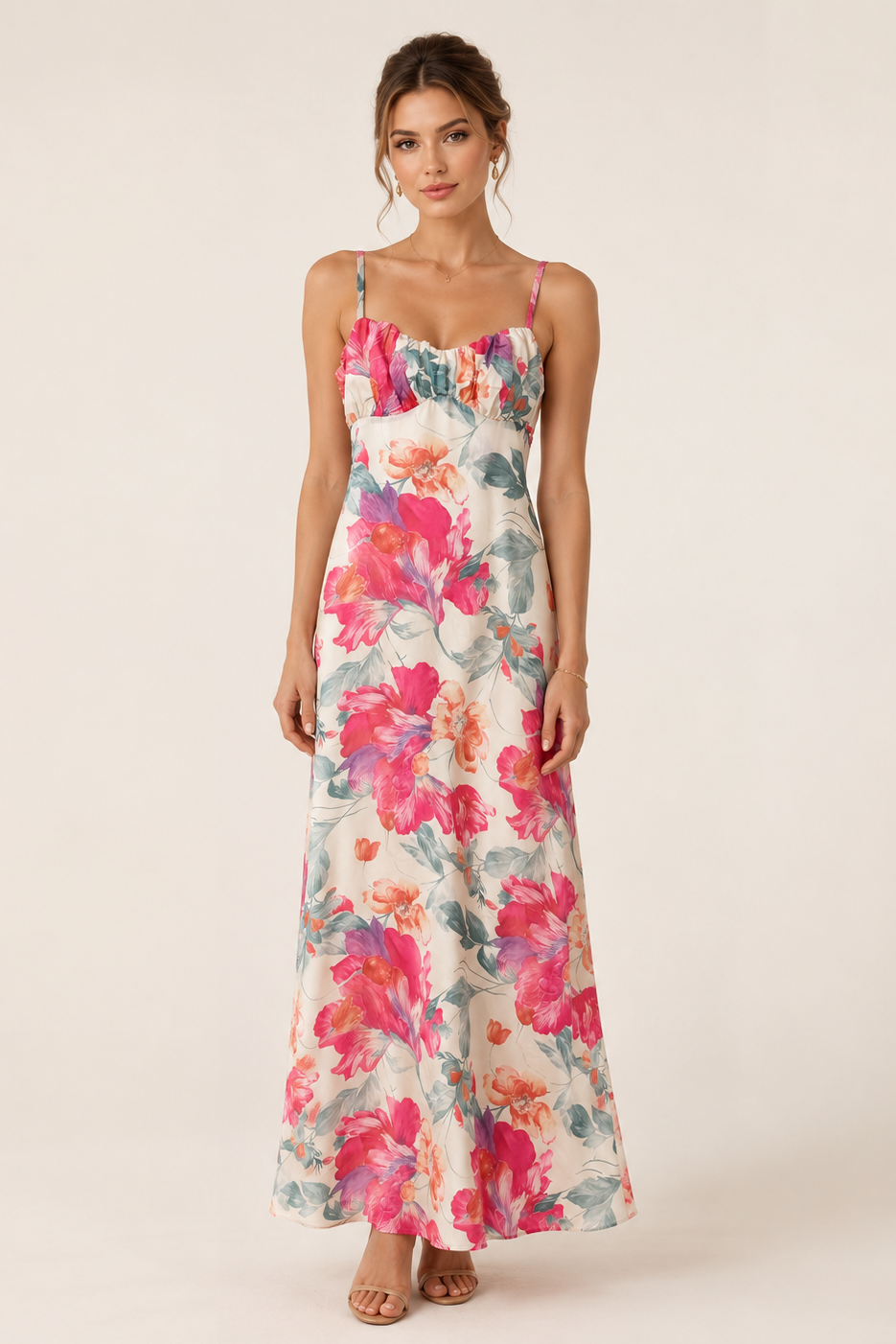 A woman modeling a sleeveless maxi dress with a vibrant pink, red, and blue floral print on a cream background, set against a plain beige studio backdrop.
