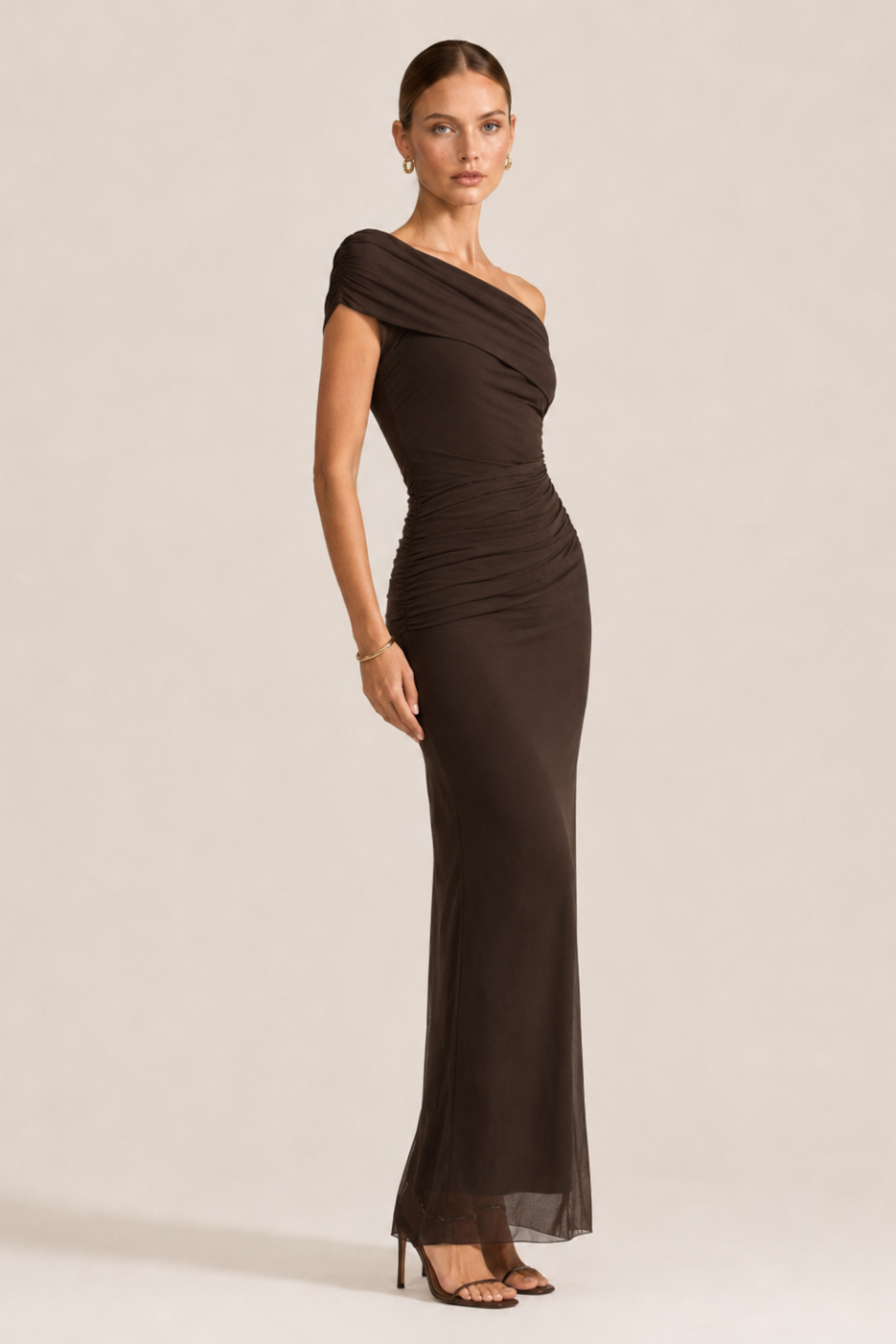 Woman wearing a brown one-shoulder evening gown against a plain background