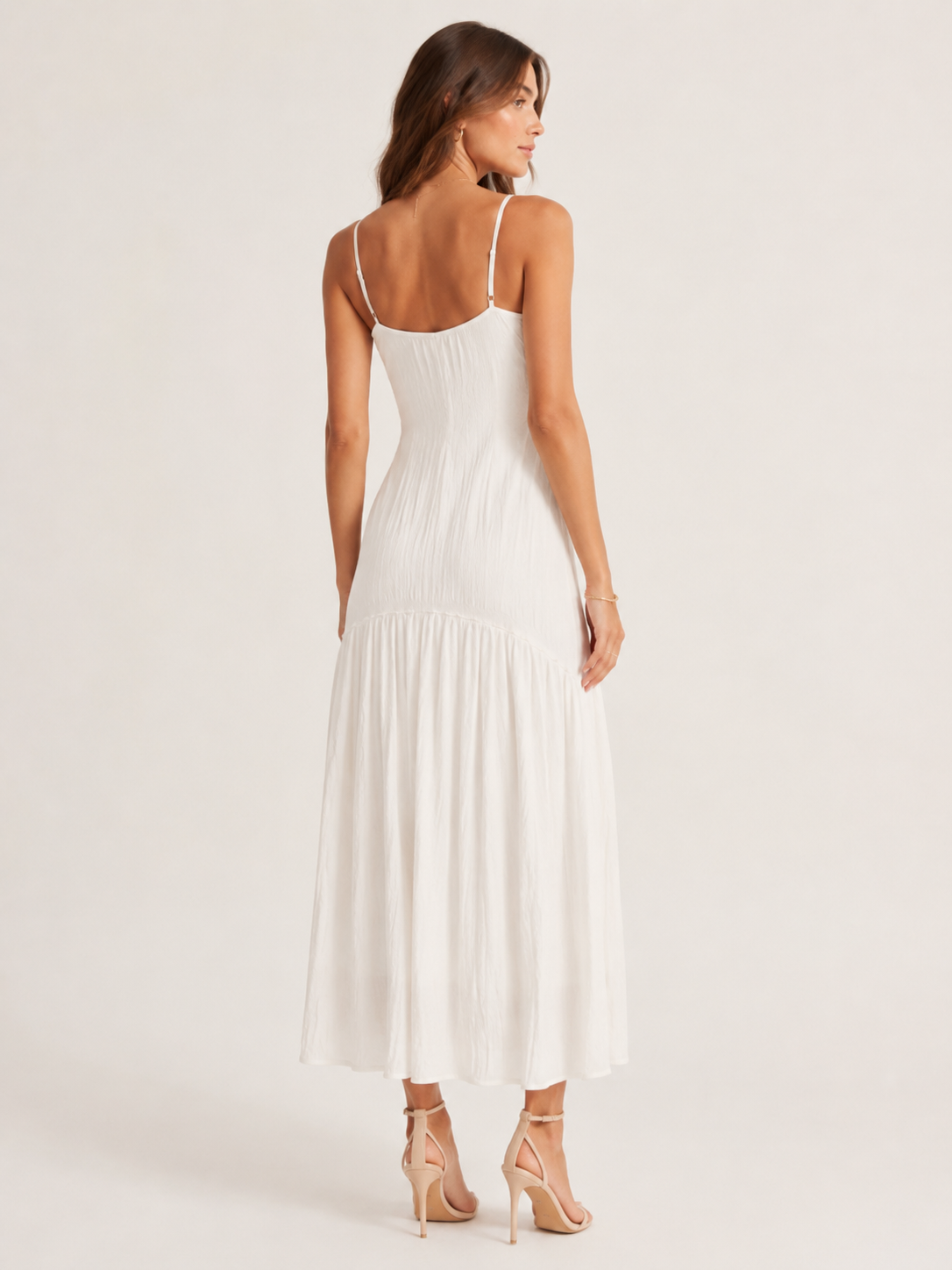 Woman wearing a white dress with thin straps on a plain background