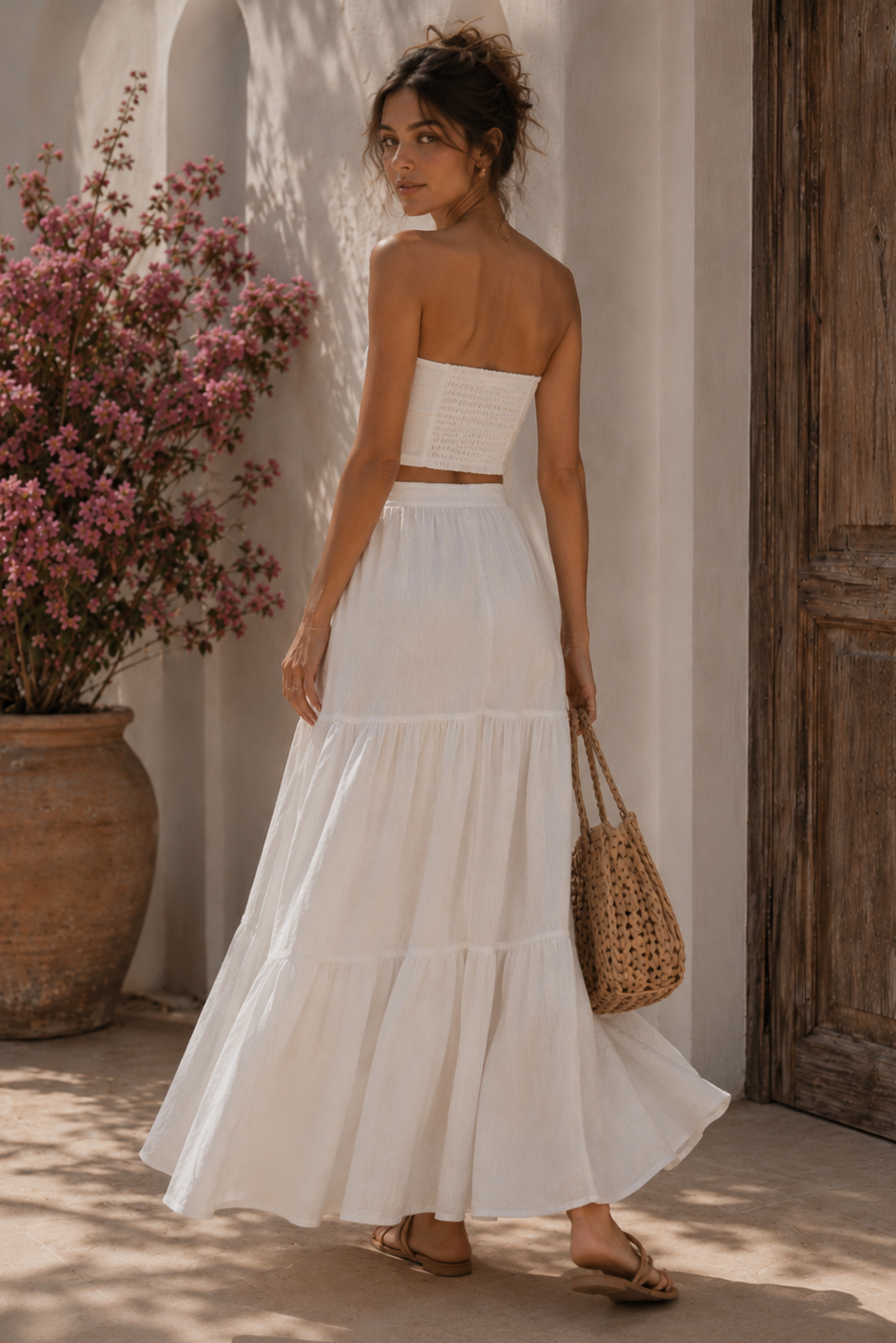 Woman in a white dress standing in front of a wooden door and potted plant.