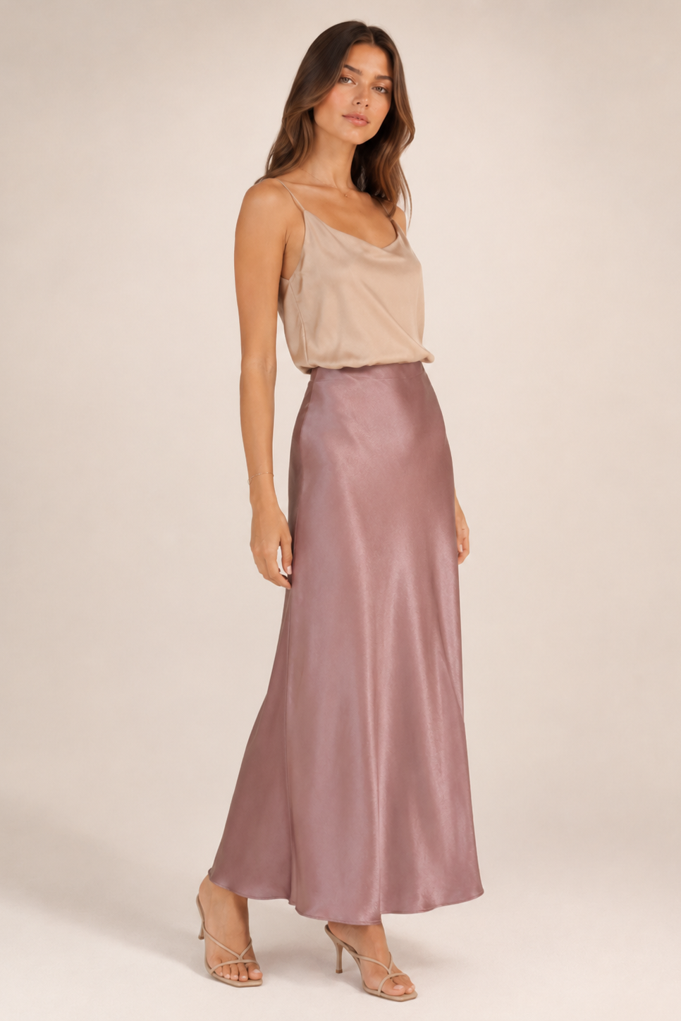 Woman wearing a beige top and pink satin skirt on a white background