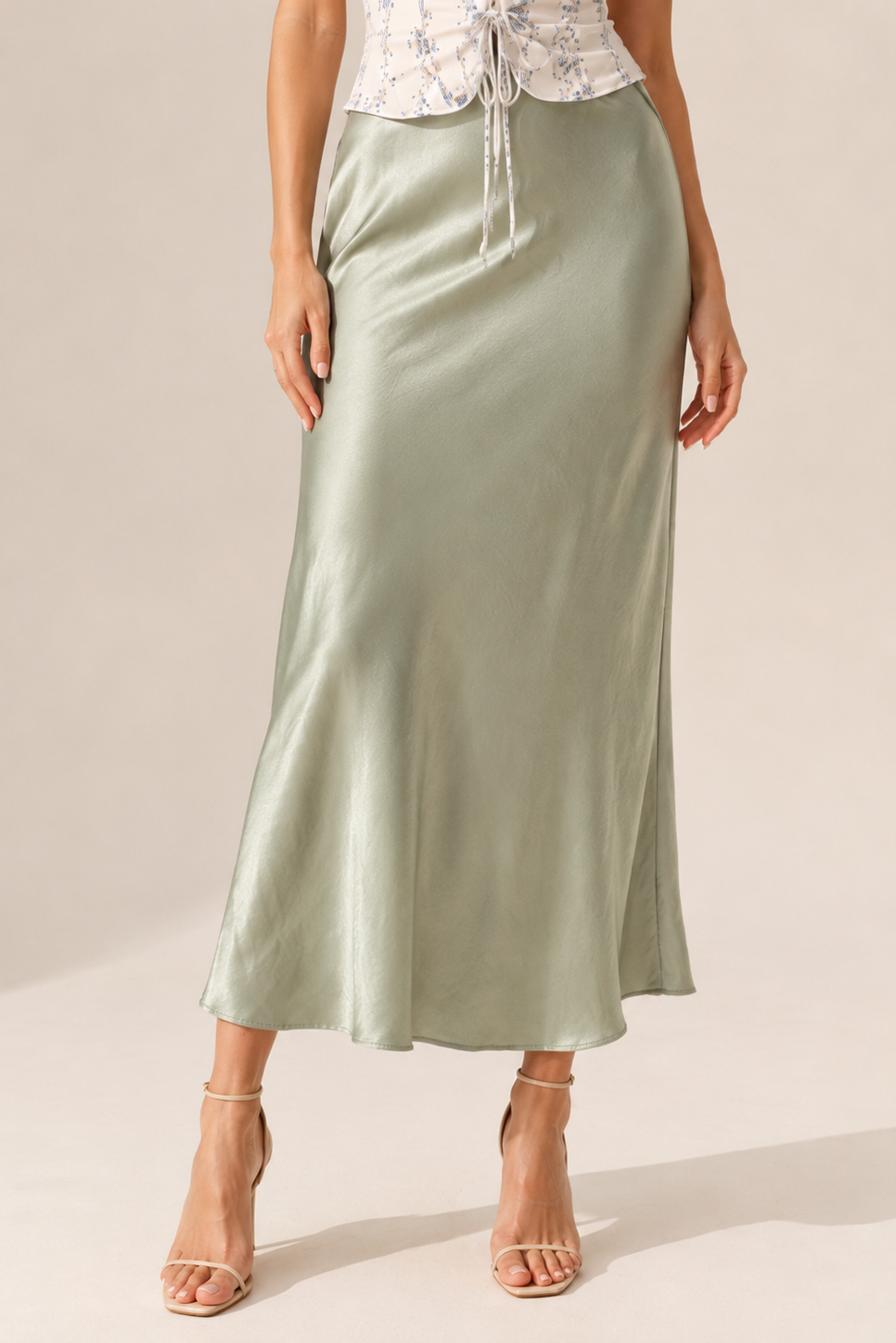 Person wearing a long green satin skirt on a plain background