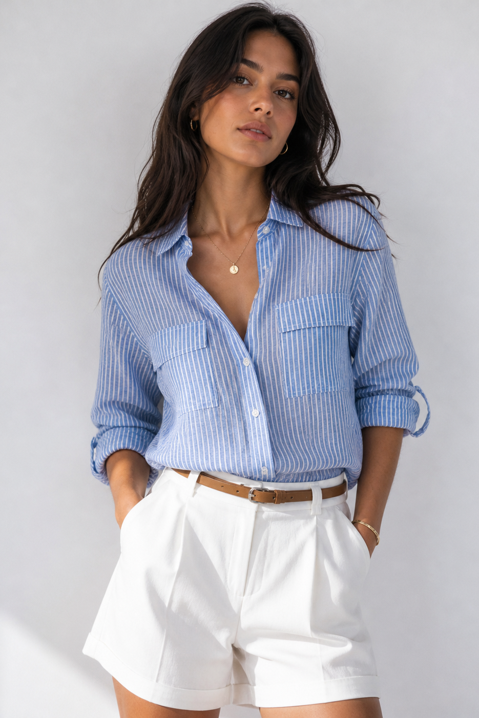 Woman wearing a blue striped shirt and white shorts on a plain background