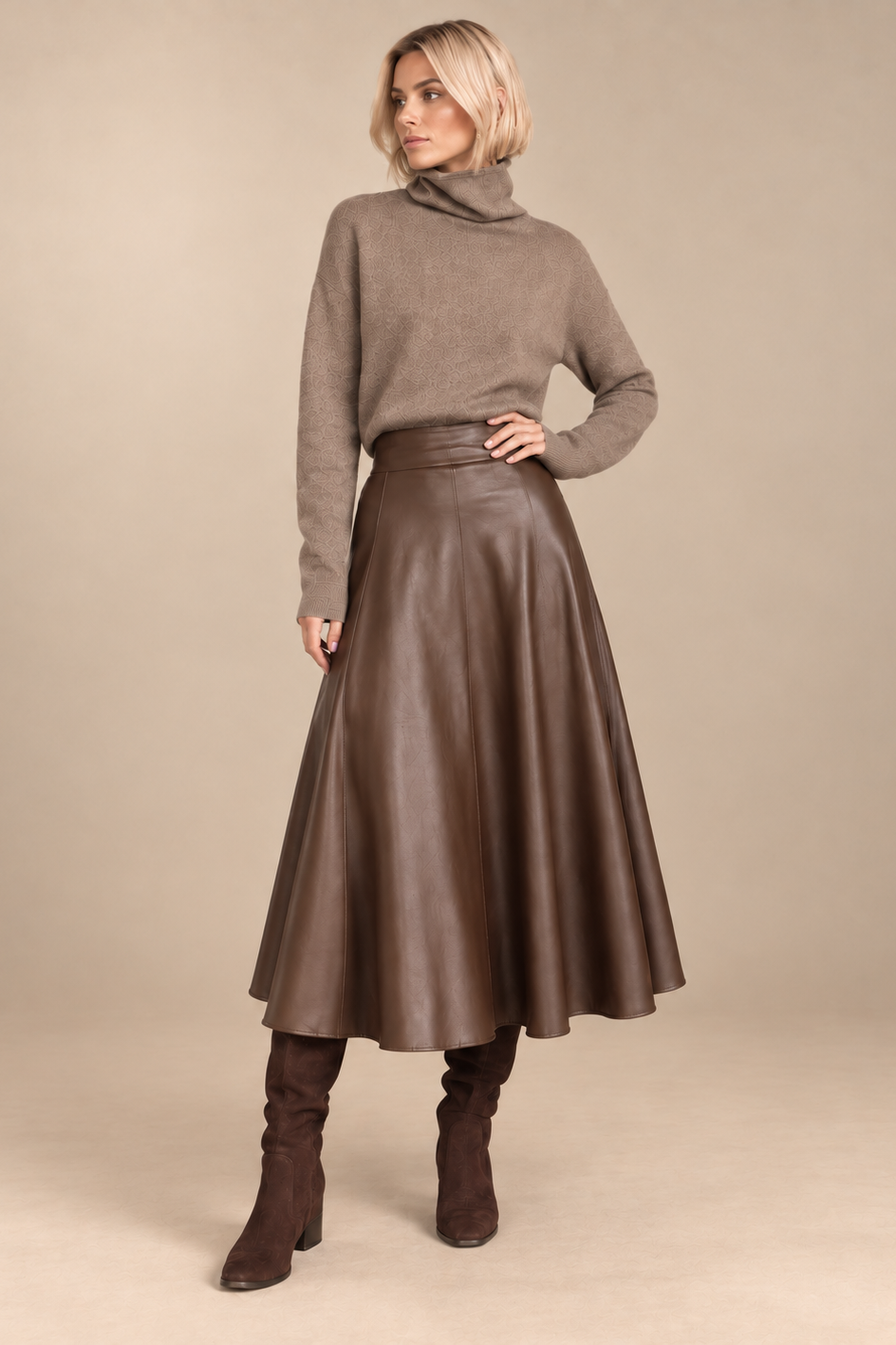A woman models a brown turtleneck sweater and a brown faux-leather A-line midi skirt, paired with brown suede knee-high boots, against a solid beige studio background.