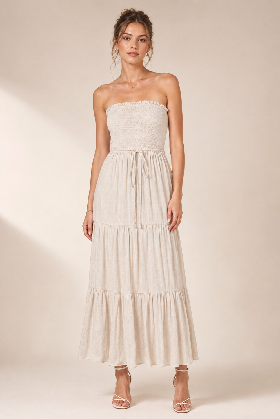 Woman wearing a strapless, tiered beige dress against a plain background