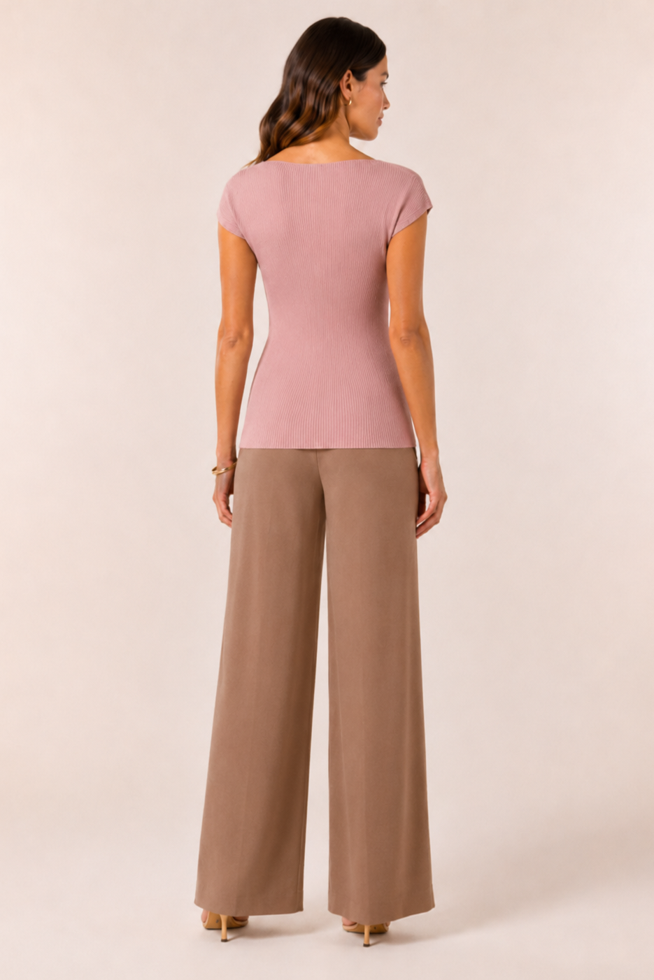 Woman wearing a pink top and brown pants on a beige background
