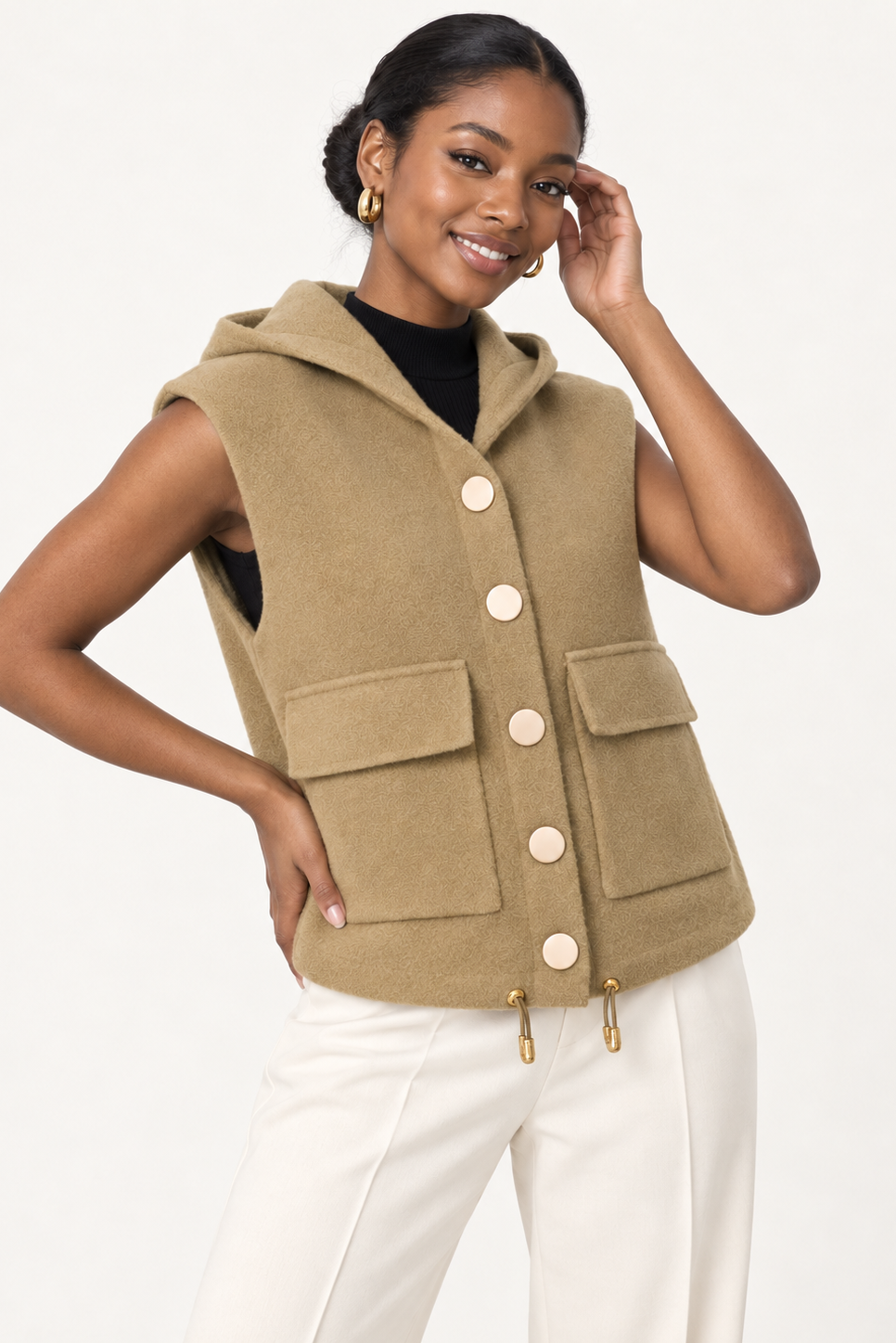 A woman modeling a sleeveless hooded vest in a warm camel beige color, featuring large front flap pockets and decorative buttons, paired with white pants and a black top against a plain white background.