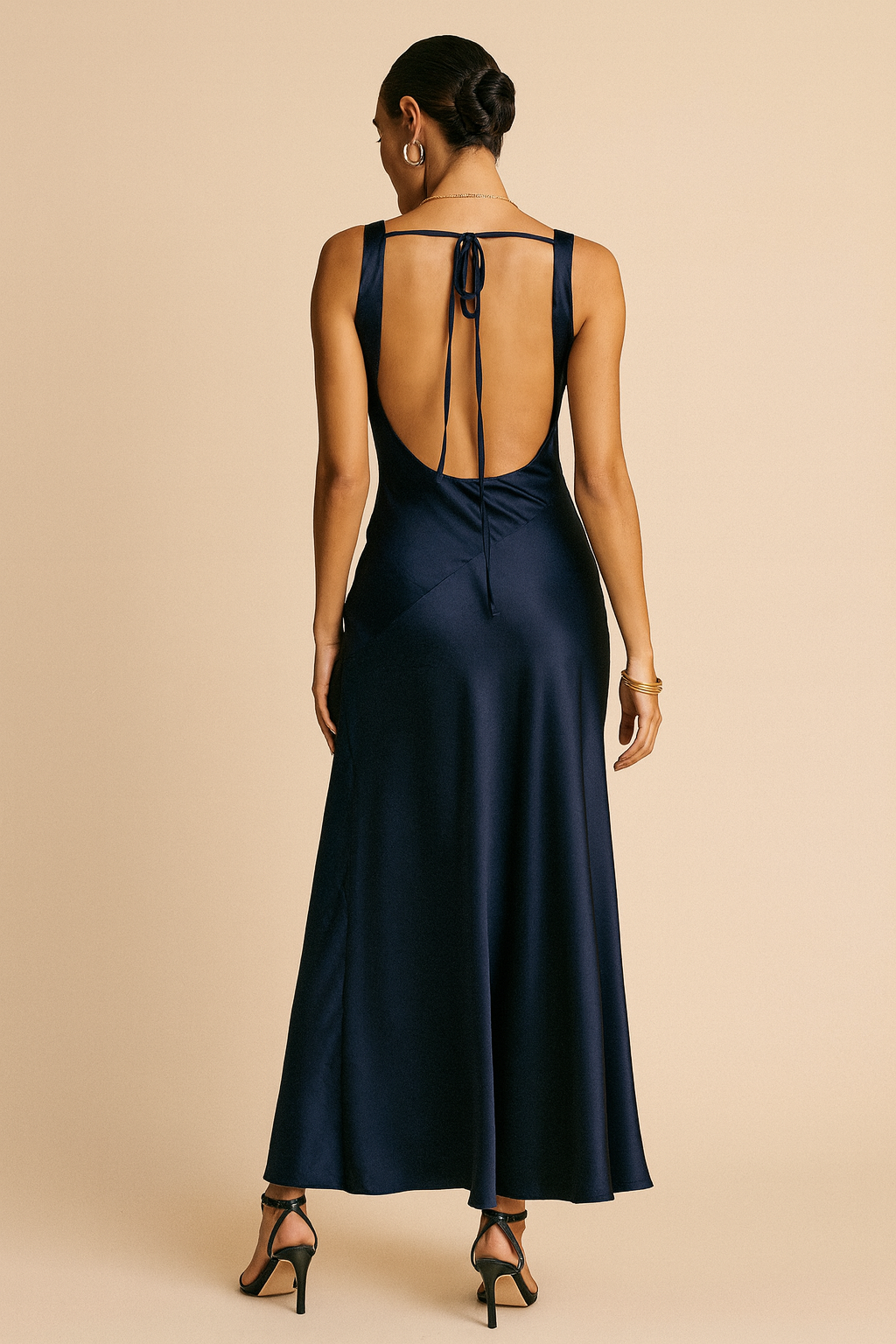 Woman wearing a navy satin maxi dress with a draped cowl neck, low open back tied at the shoulders, and a flared hem.