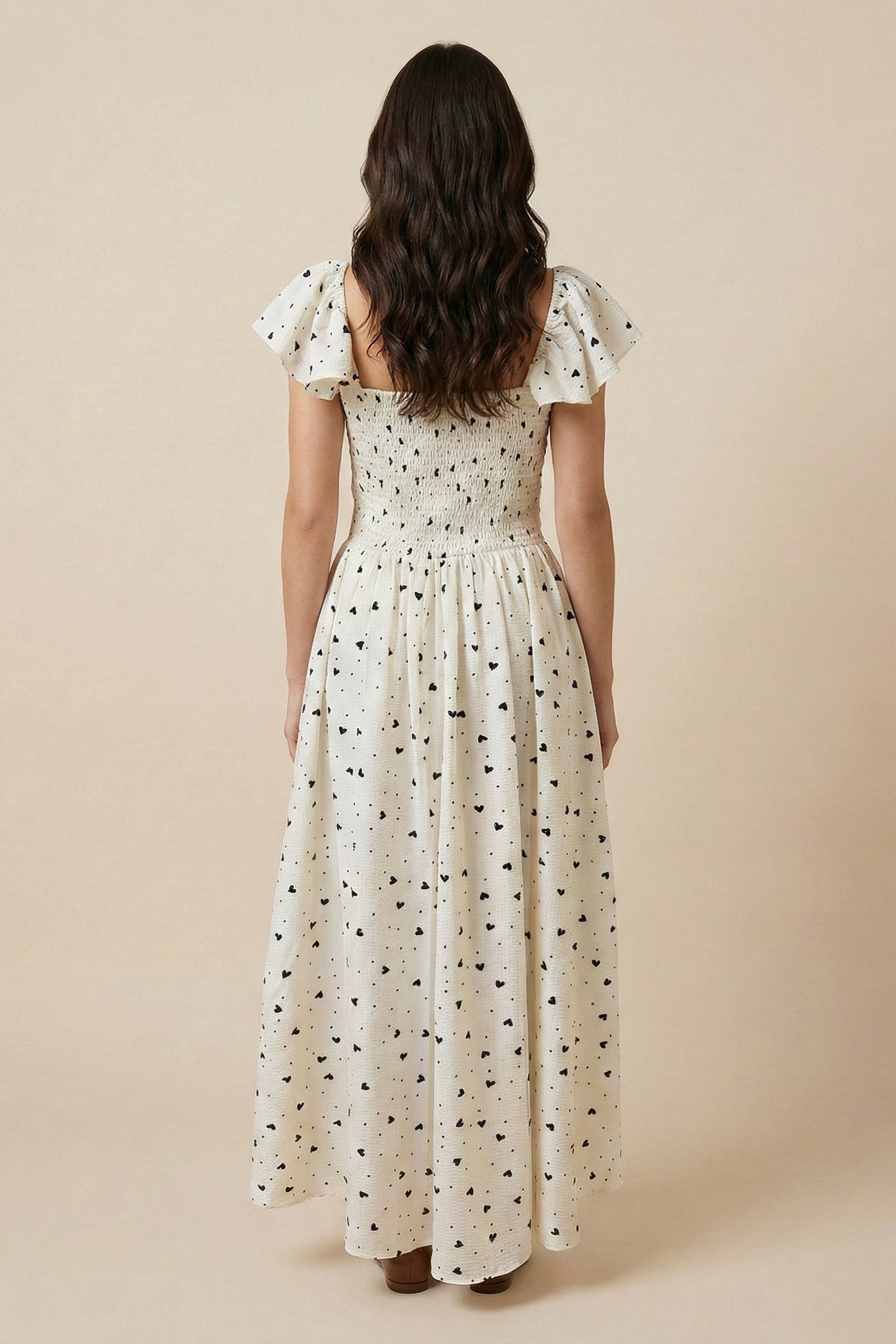 Woman wearing a white dress with black polka dots against a beige background