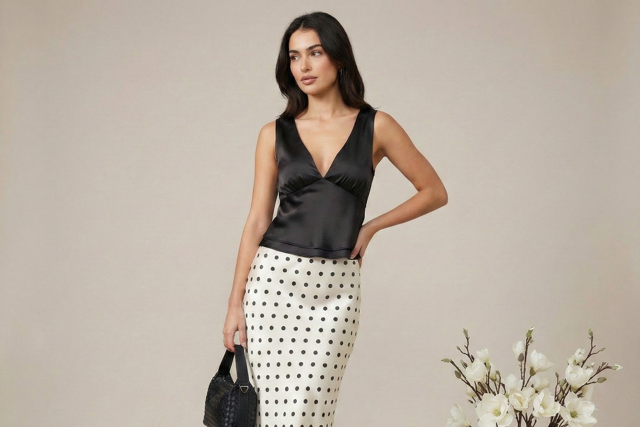Woman wearing a black top and polka dot skirt with a vase of flowers on a neutral background