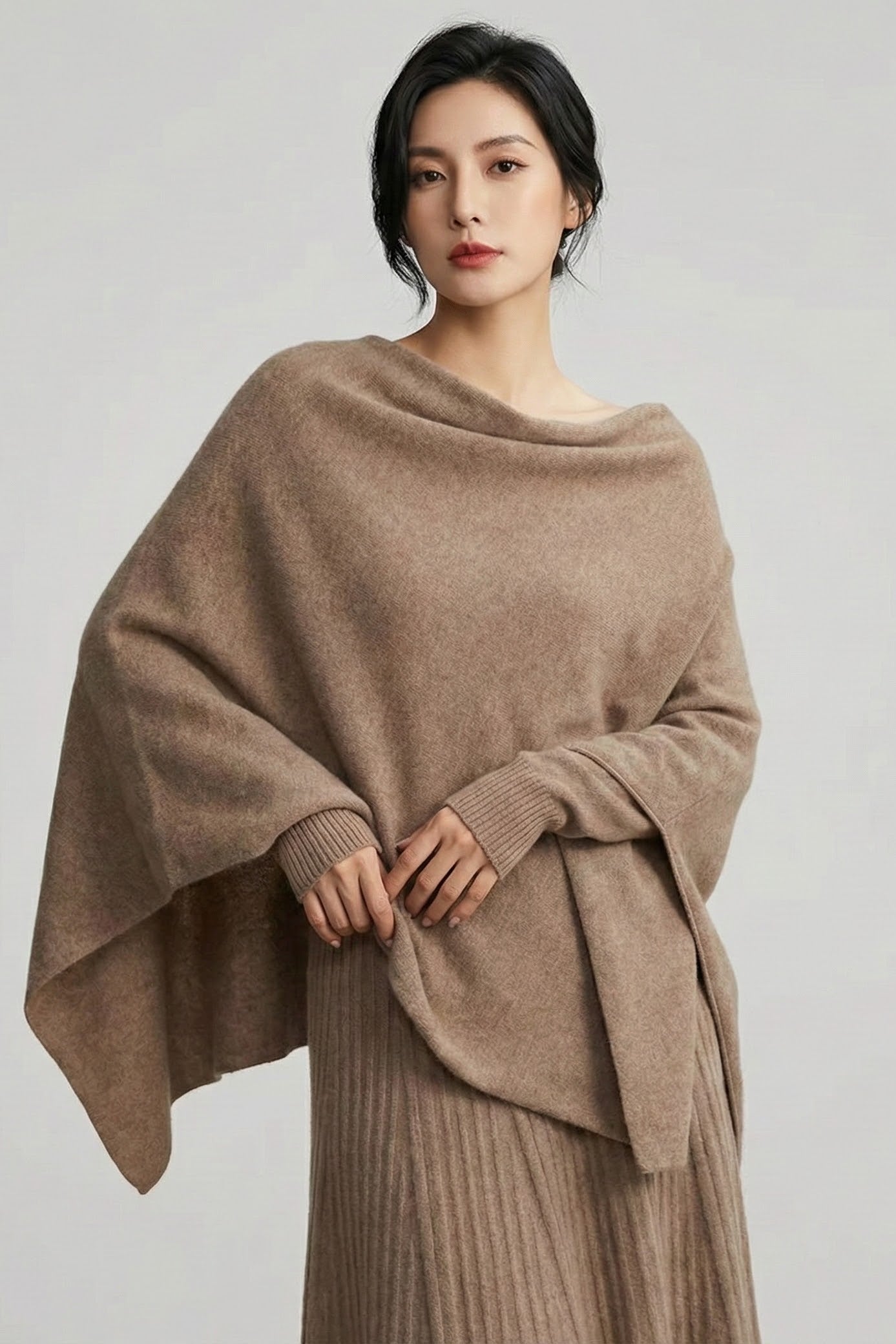 Woman wearing a beige poncho over a dress on a plain background