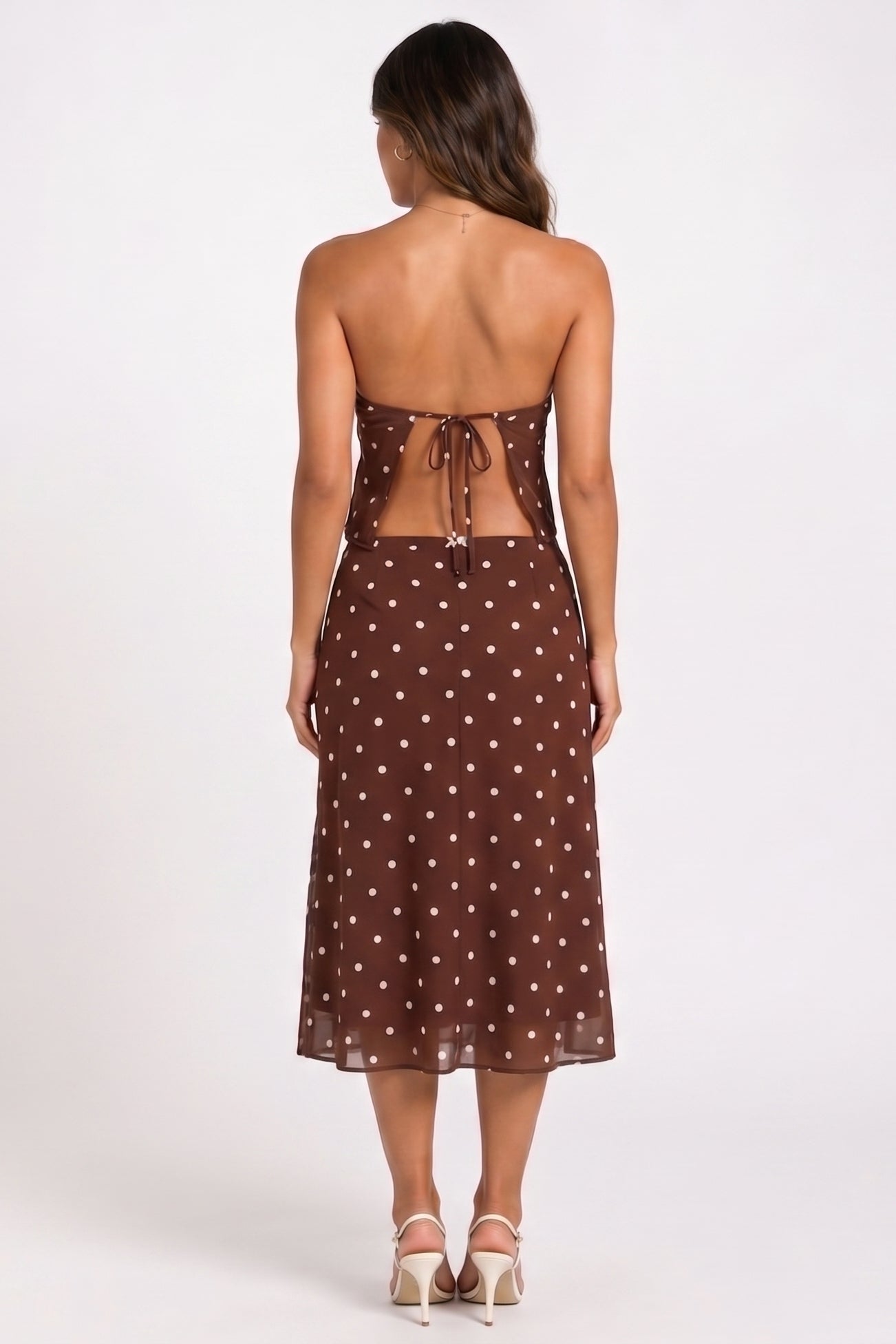 Woman wearing a brown strapless dress with white polka dots on a white background