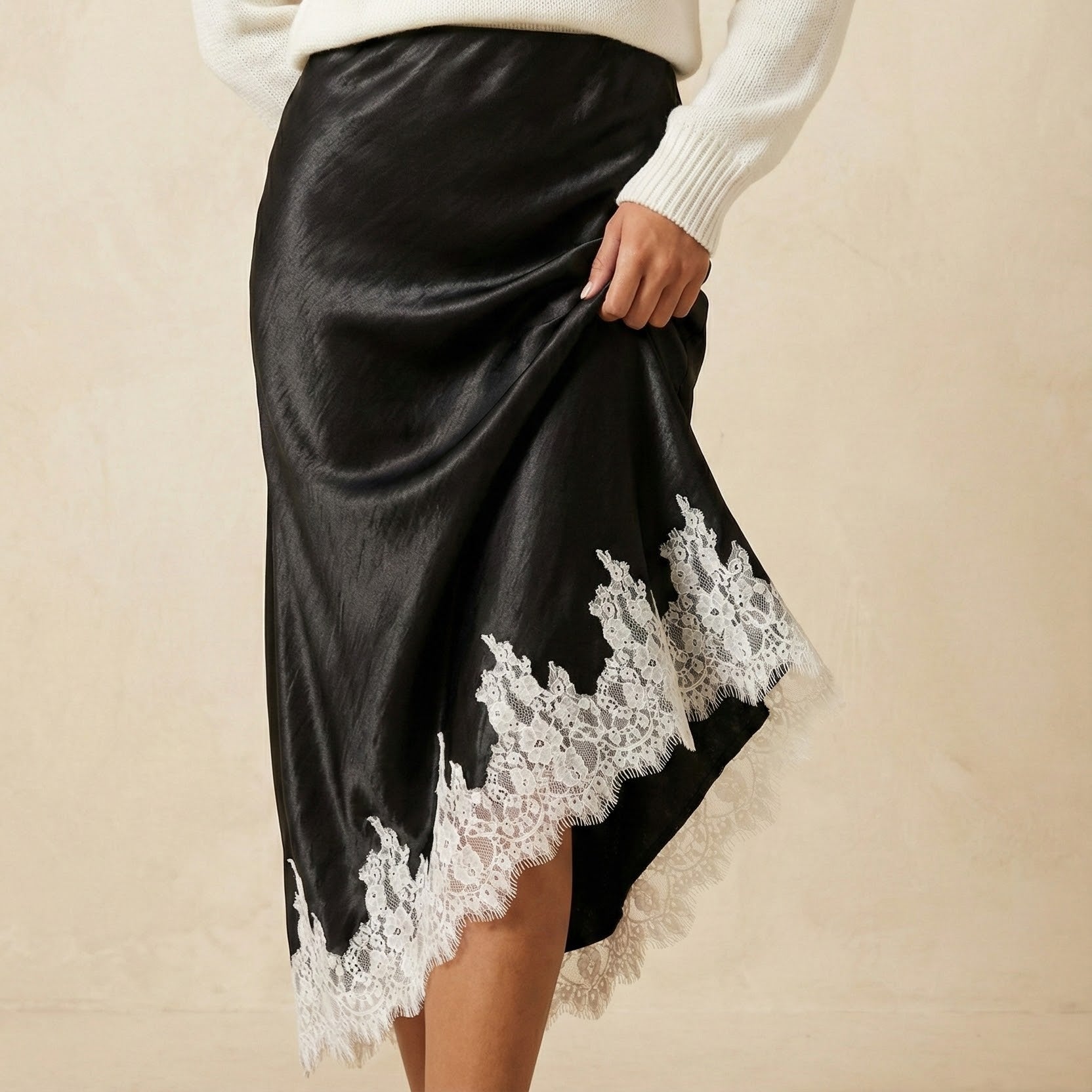Woman wearing a white sweater and black satin skirt with lace trim on a beige background