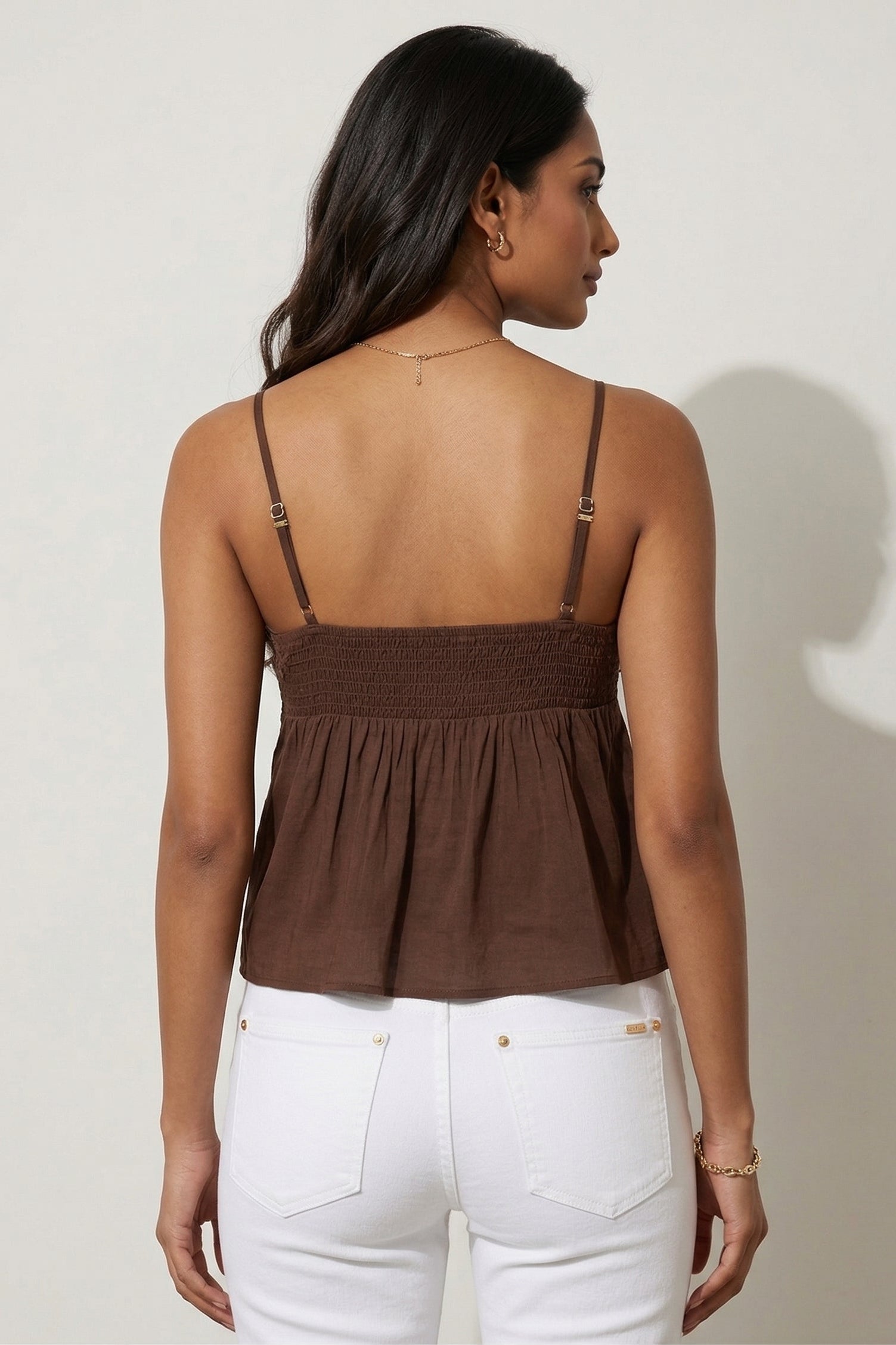 Woman wearing a brown top and white pants against a plain background