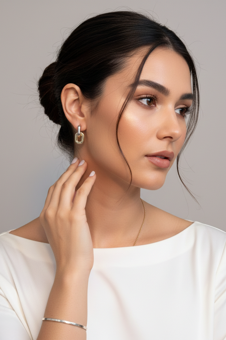 Woman wearing gold earrings and a silver bracelet against a neutral background