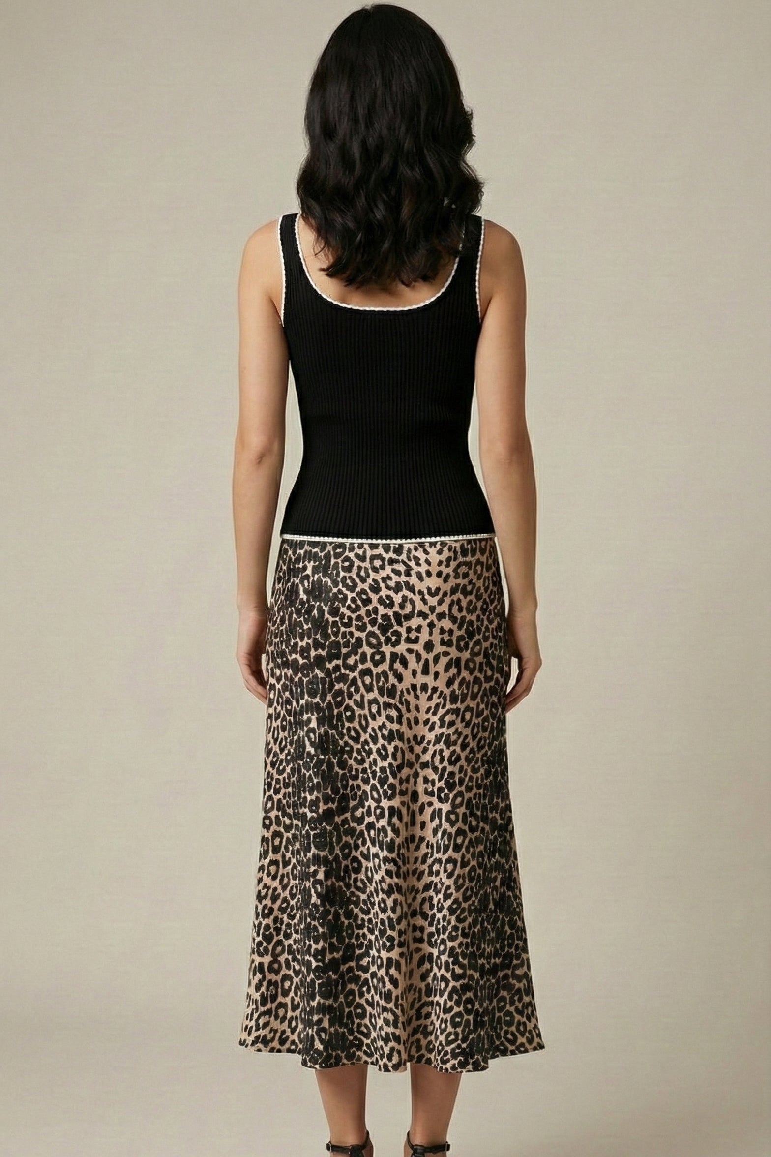 Woman wearing a black tank top and leopard print skirt on a beige background