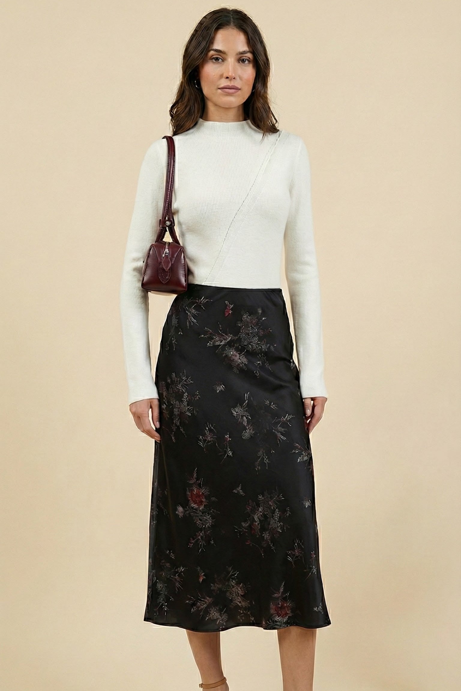 Woman wearing a white long-sleeve top and black floral skirt on a beige background