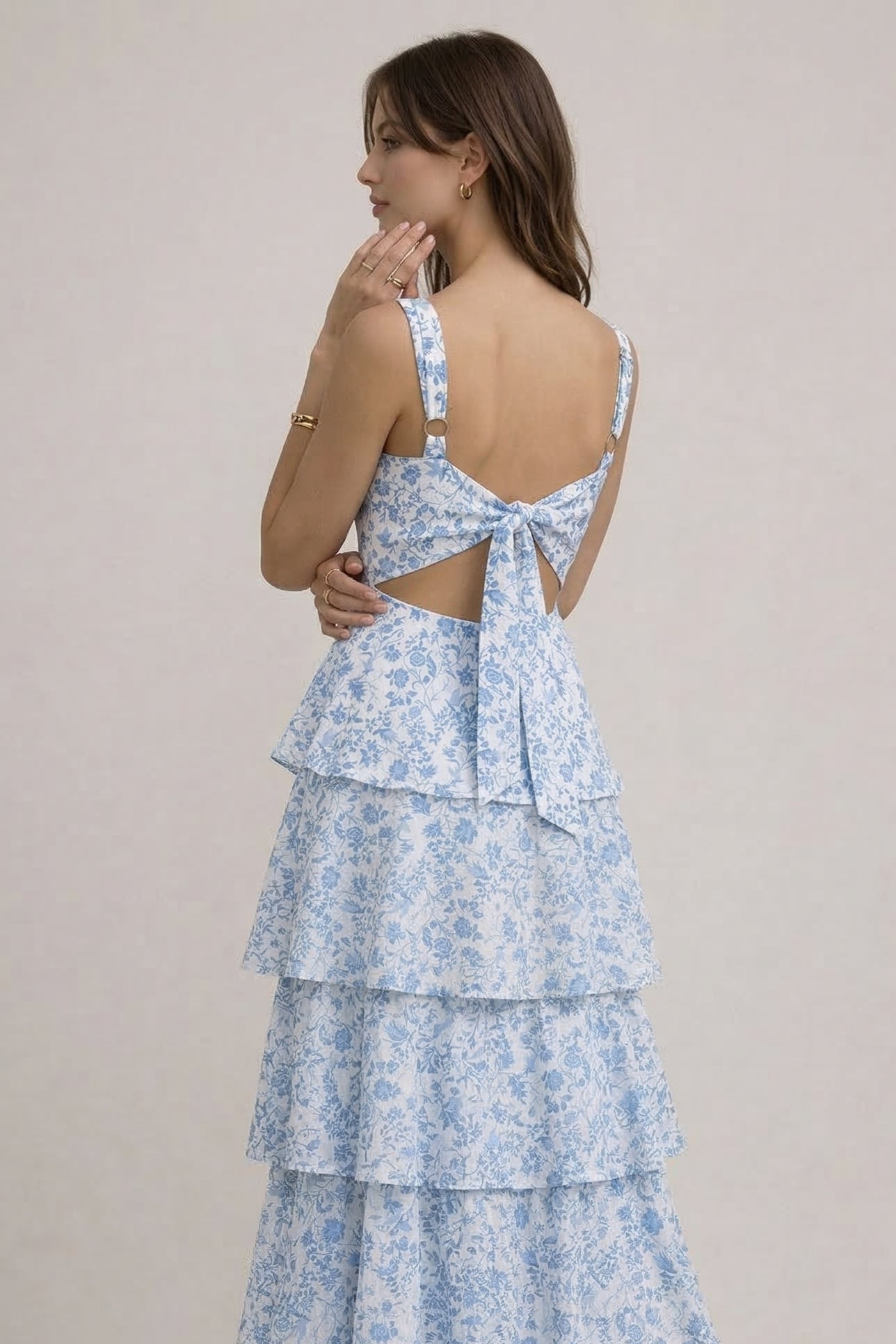 Woman wearing a light blue floral dress with tiered layers on a beige background