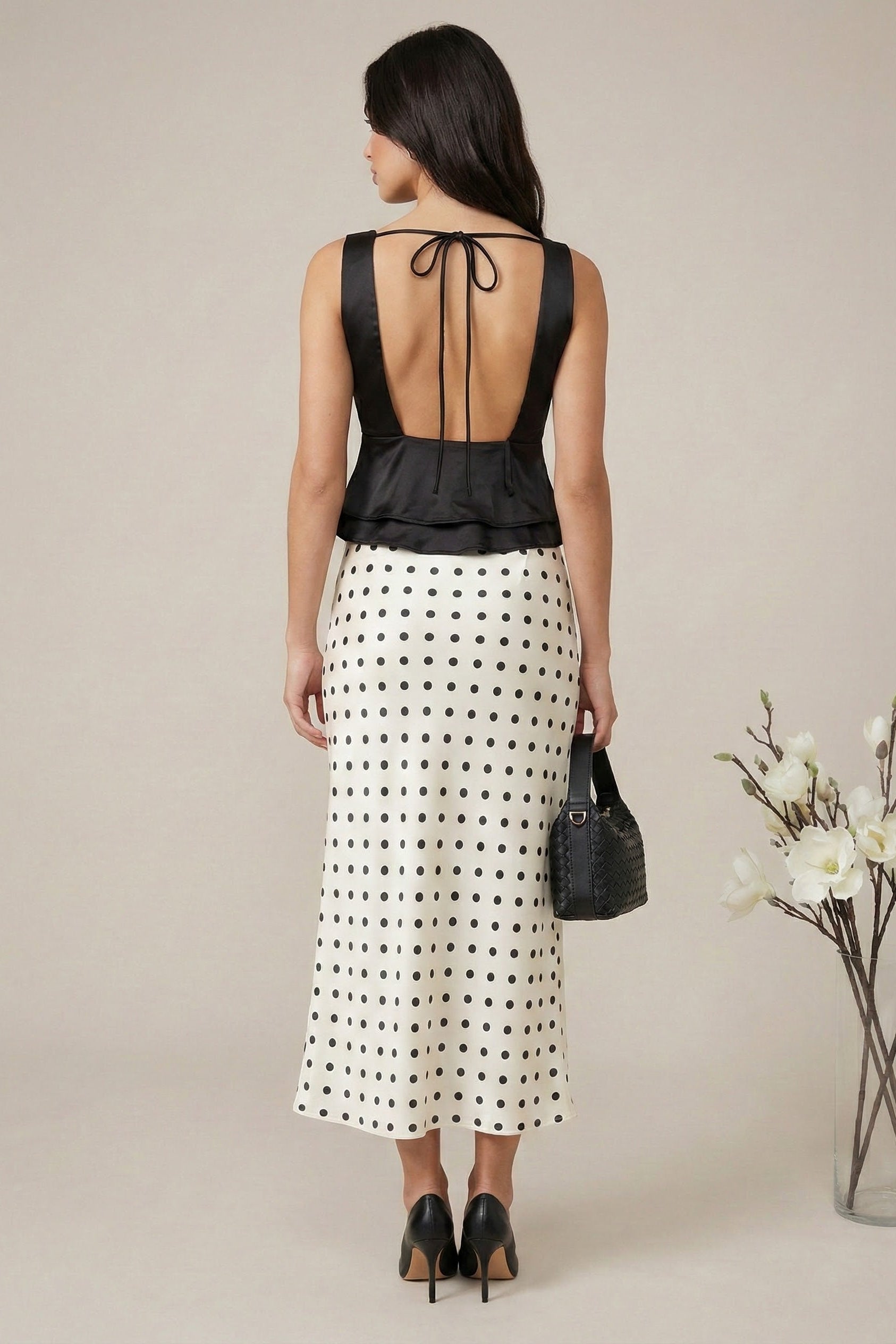 Woman wearing a black top with open back and white polka dot skirt, holding a black handbag.
