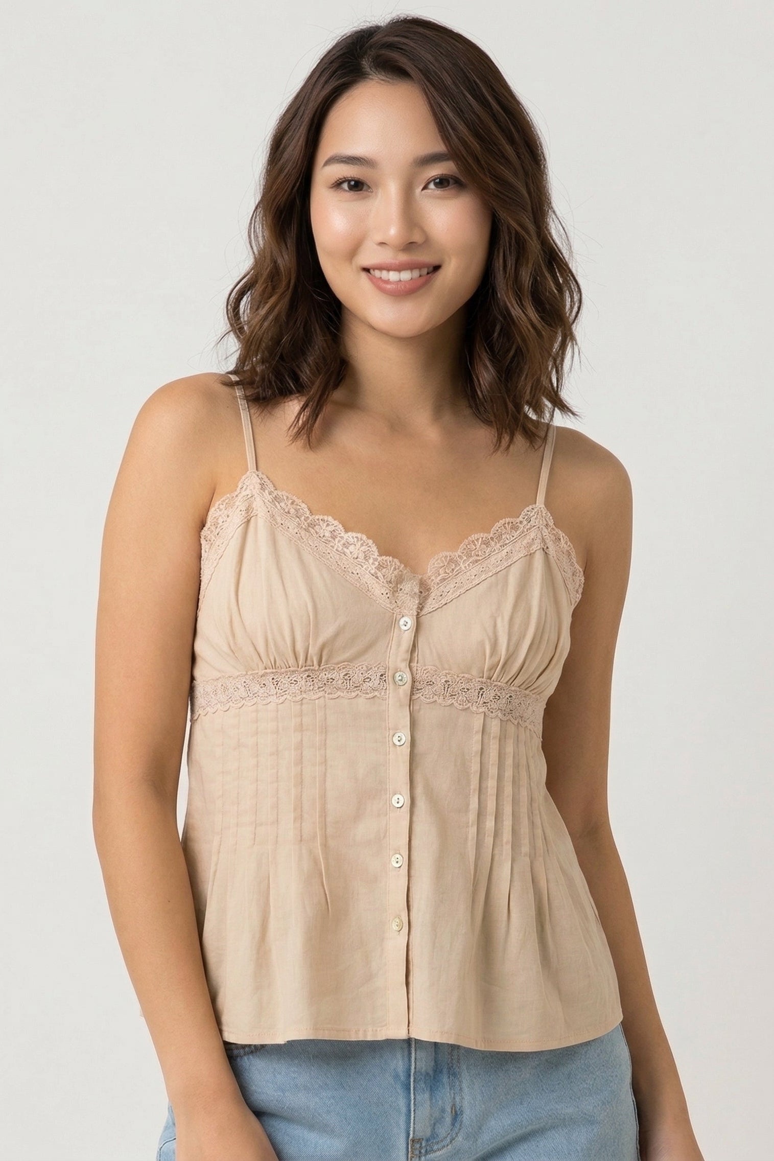 Woman wearing a beige lace-trimmed top against a plain background