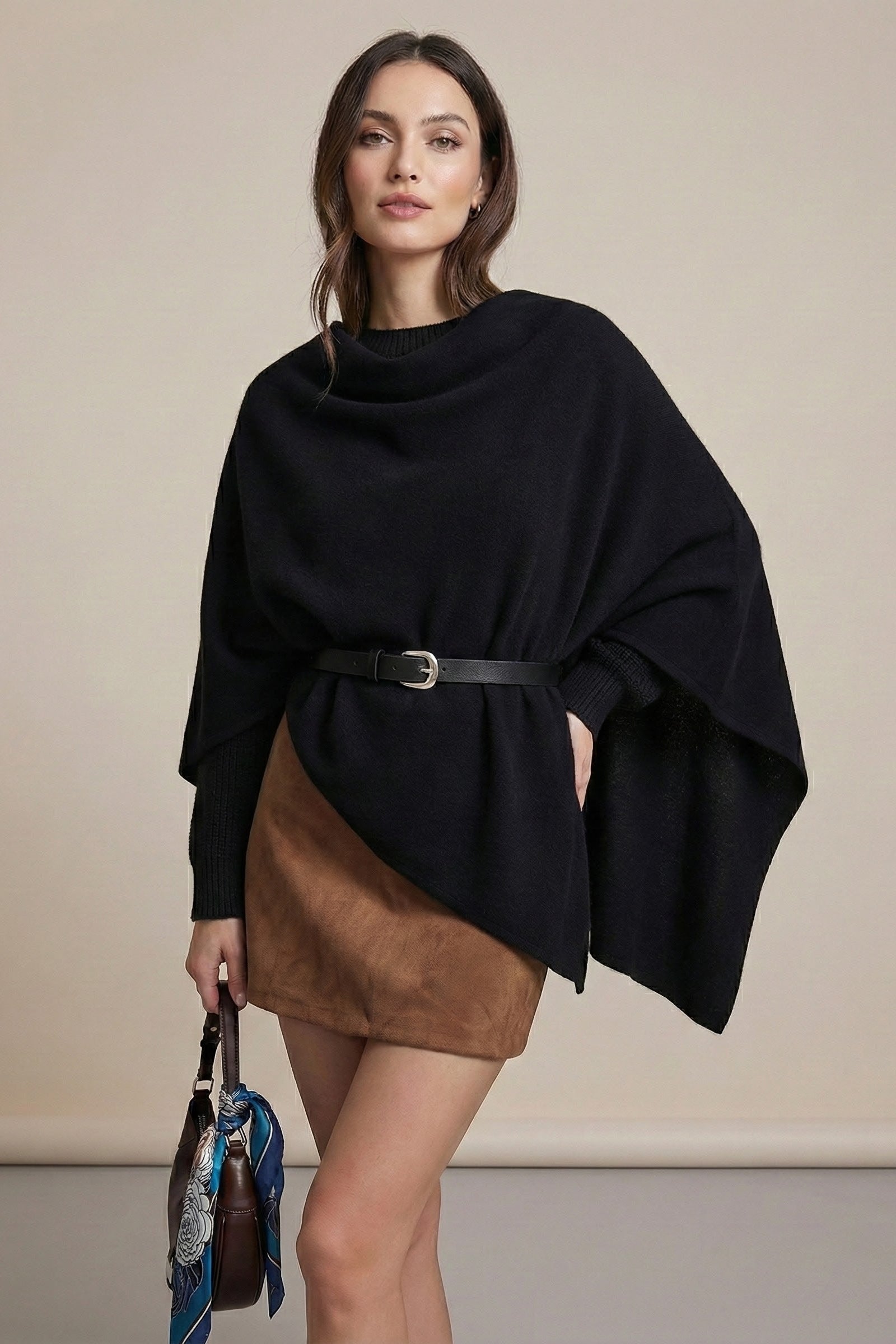 Woman wearing a black poncho over a brown skirt with a beige background