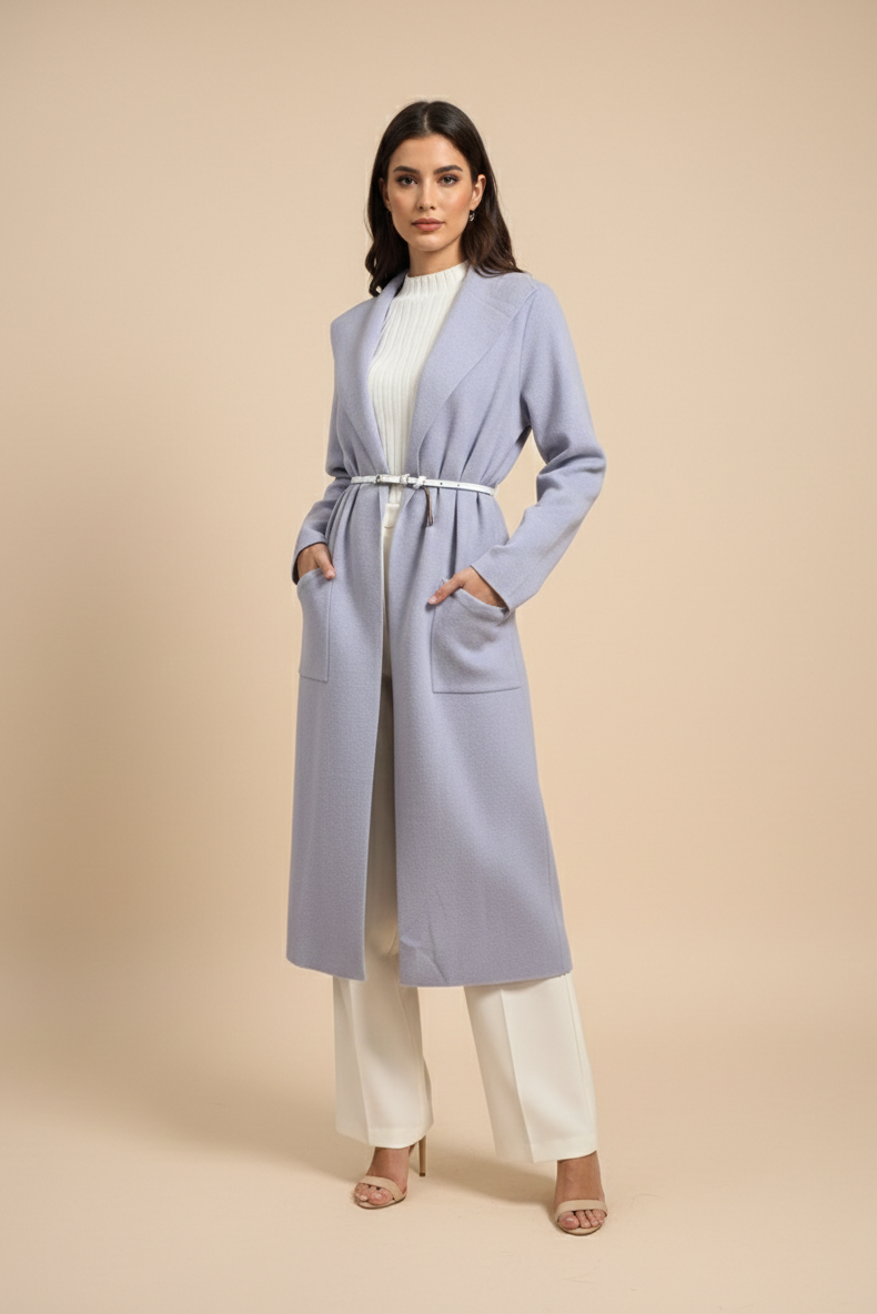 Woman wearing a long light blue coat over a white outfit on a beige background