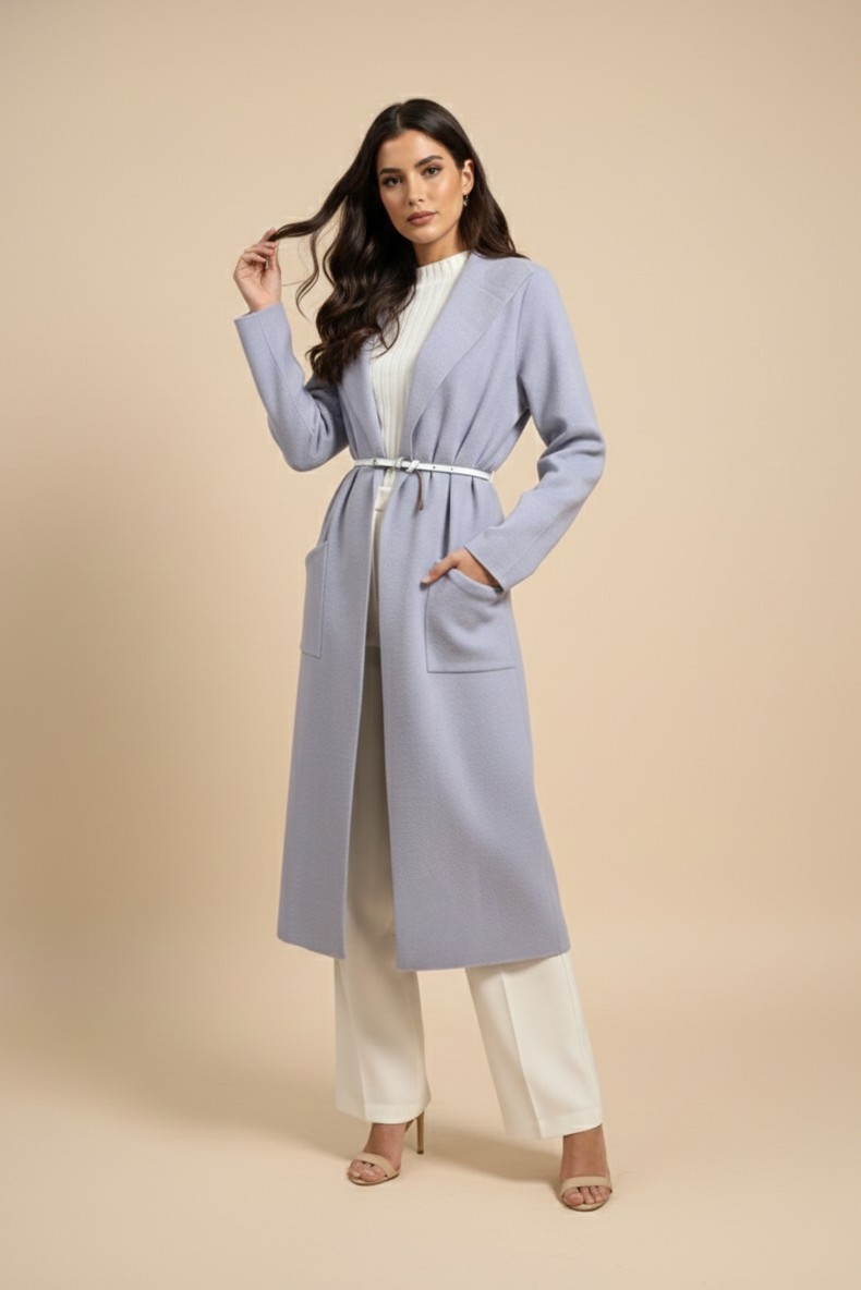 Woman wearing a long light blue coat over a white outfit on a beige background