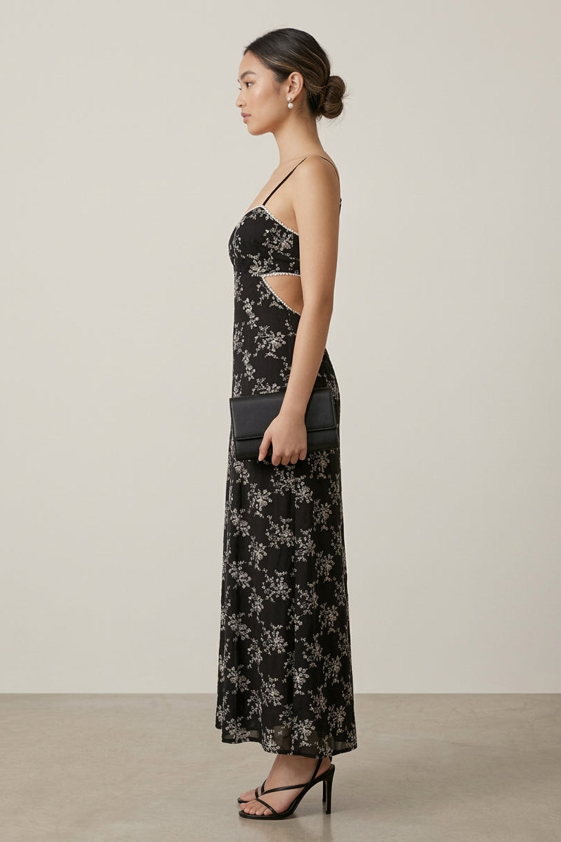 Woman wearing a black floral dress with cut-out details on a plain background