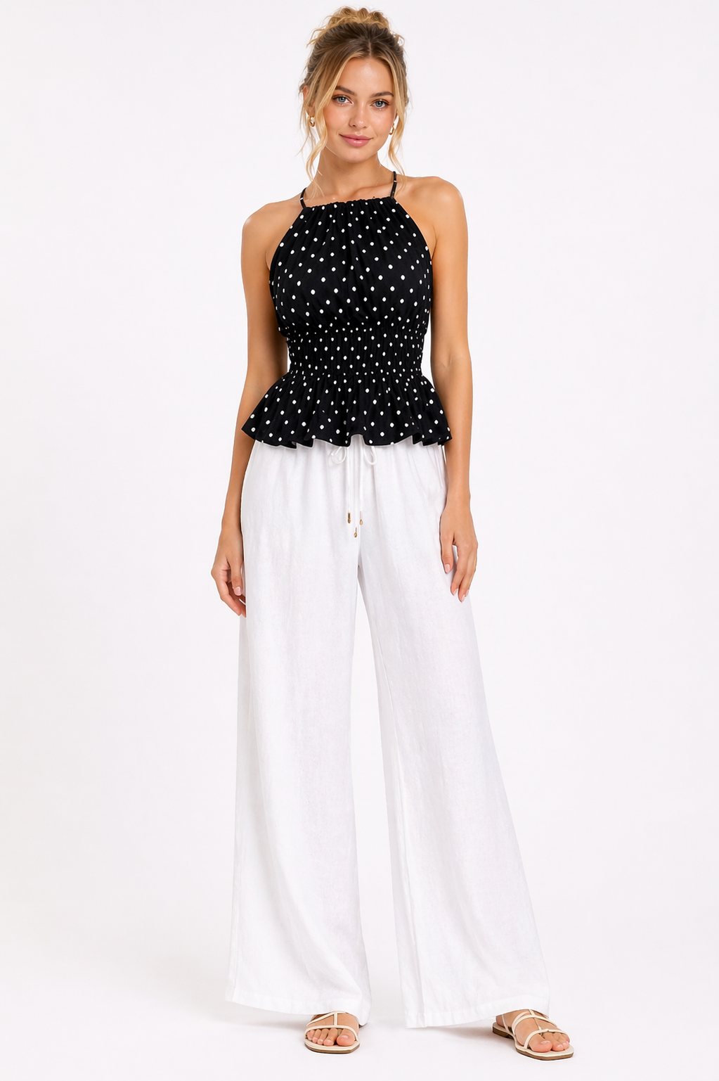 Woman wearing a black polka dot top and white pants on a white background