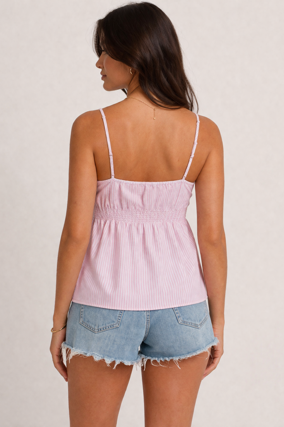Woman wearing a pink striped top and denim shorts on a plain background