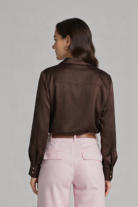 Woman wearing a brown satin shirt and pink pants on a plain background