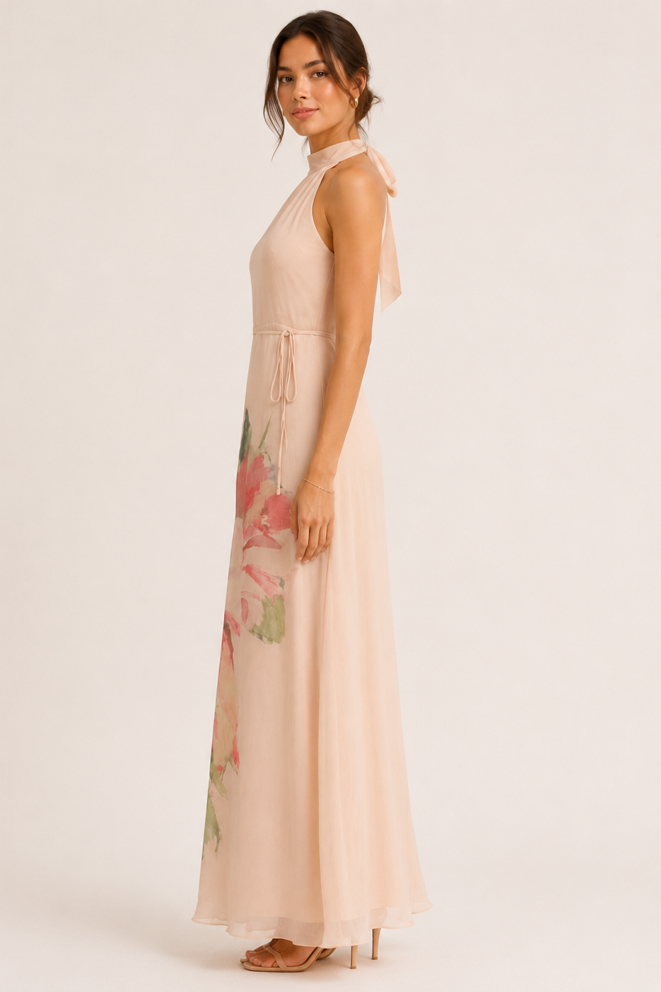 Woman wearing a long, light-colored dress with floral patterns on a plain background