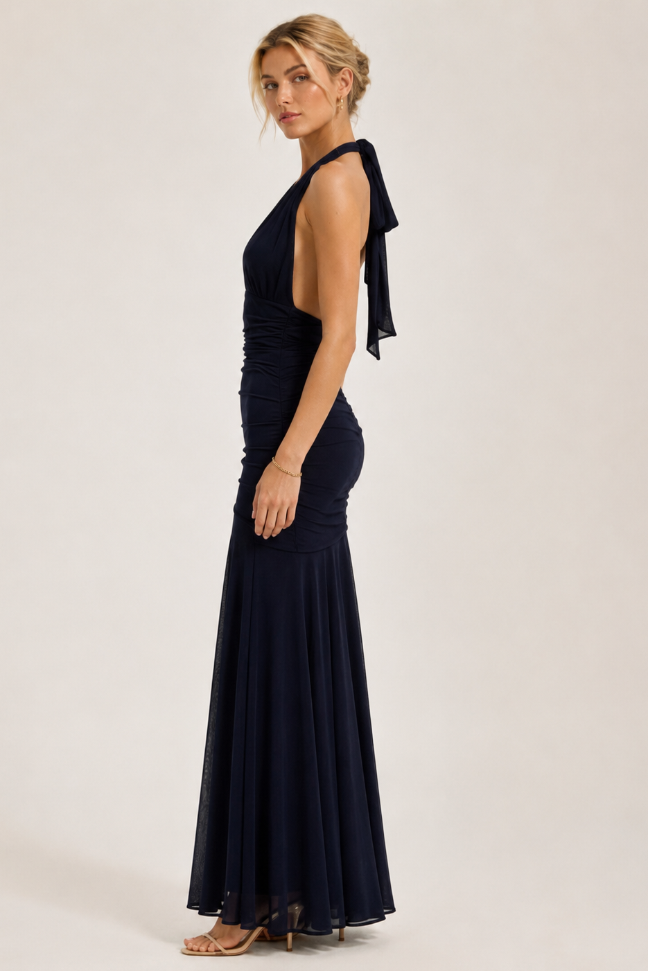 Woman wearing a navy blue evening gown with a halter neck design on a white background