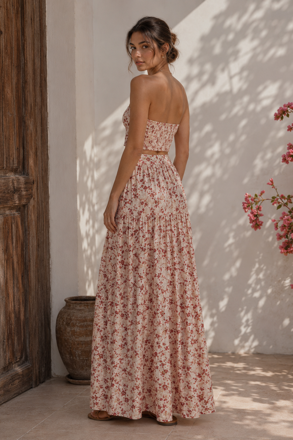 Woman in a floral dress standing in a sunlit room with a wooden door and plant.