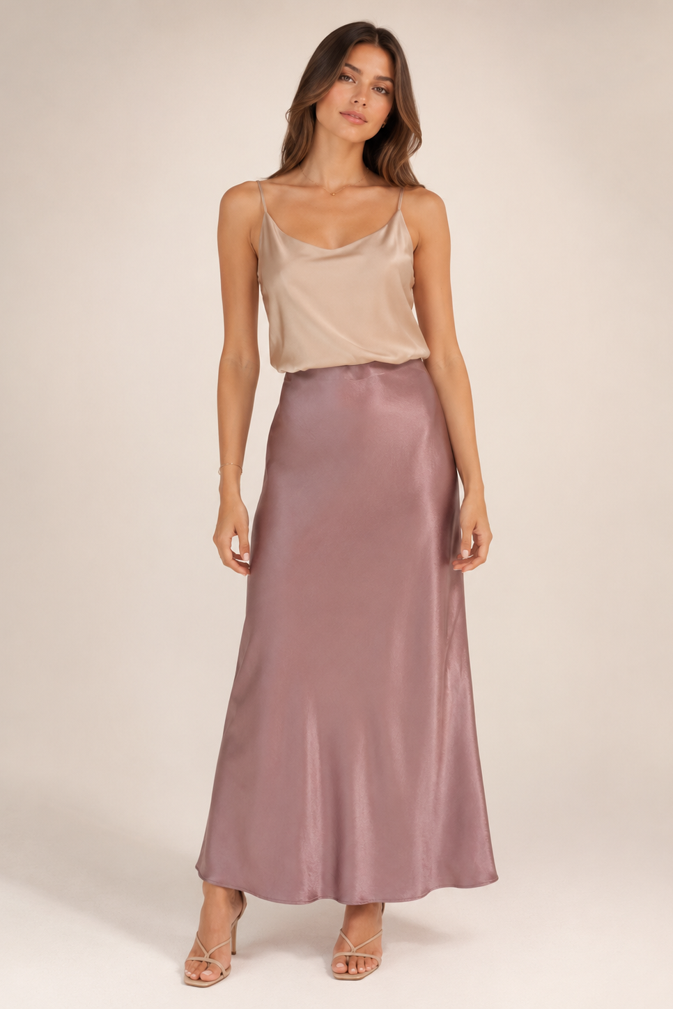 Woman wearing a beige top and long mauve skirt on a plain background