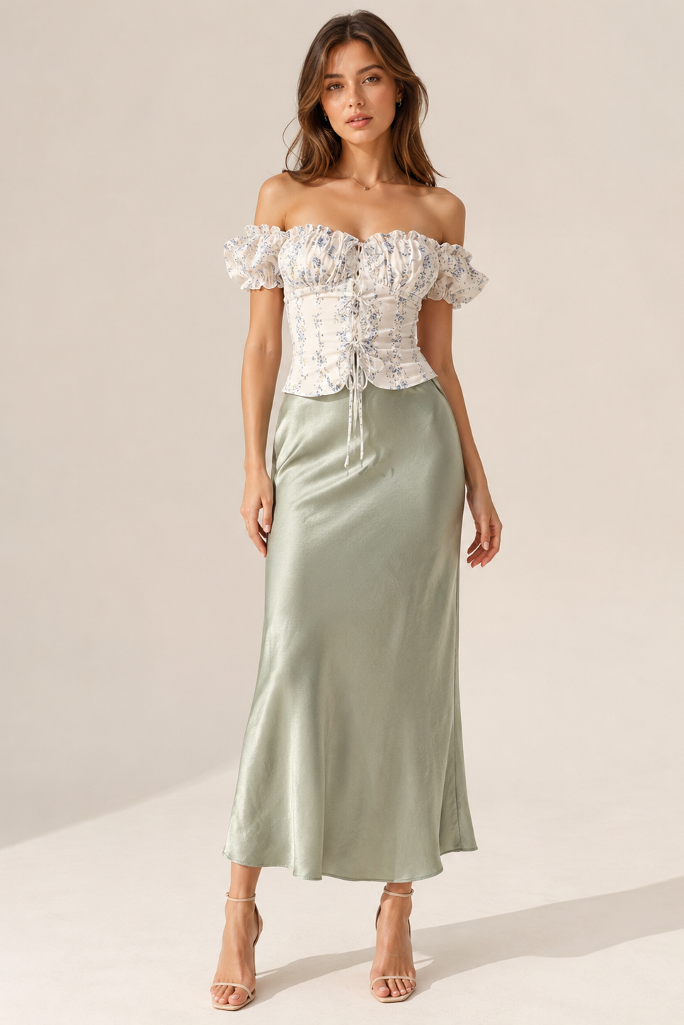 Woman wearing a white floral top and green satin skirt on a plain background