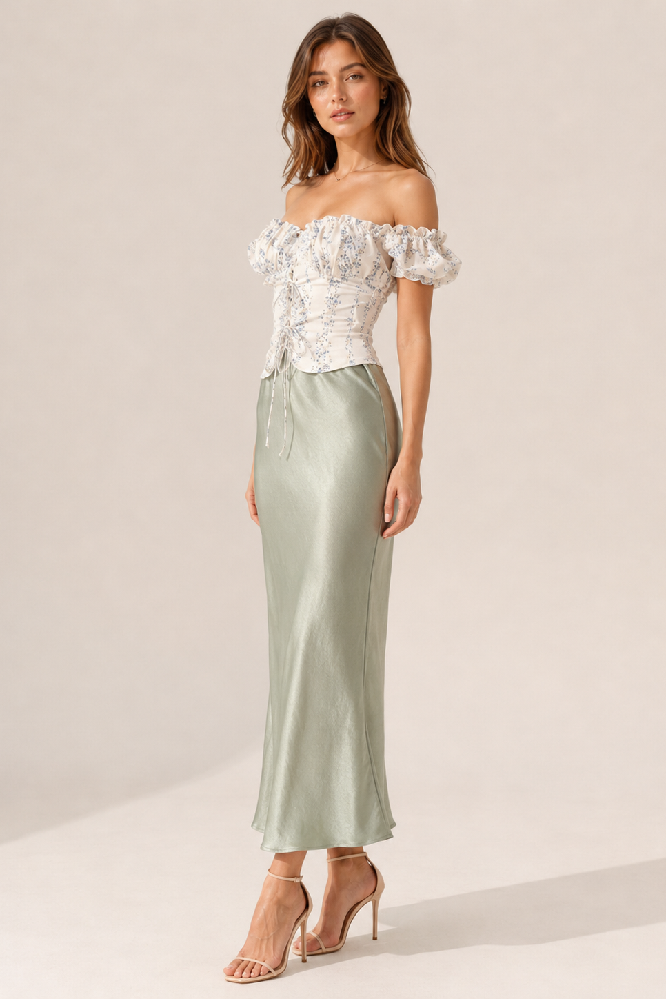 Woman wearing a white off-shoulder top and light green satin skirt on a plain background