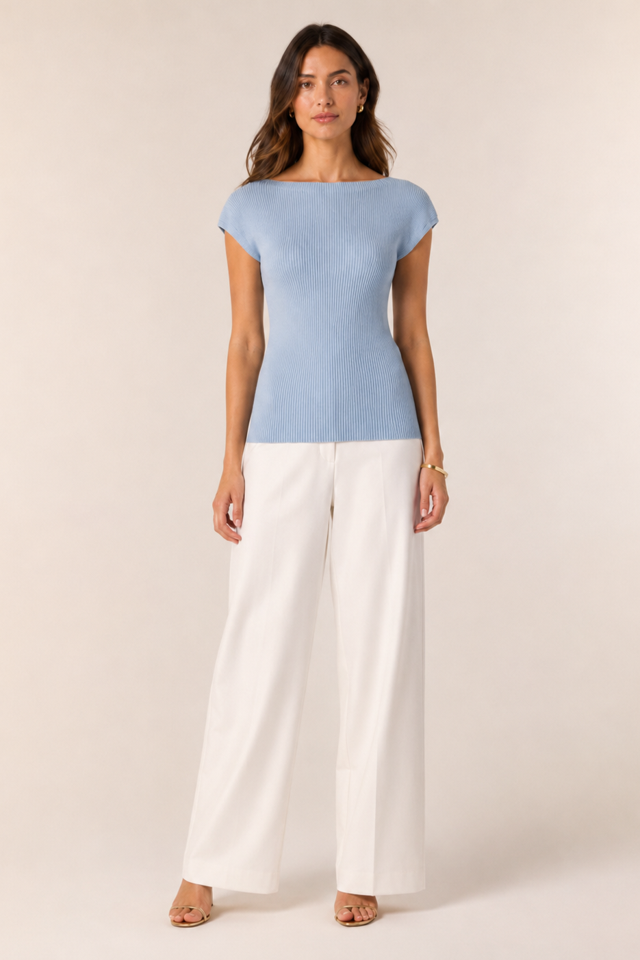 Woman wearing a light blue top and white pants on a plain background