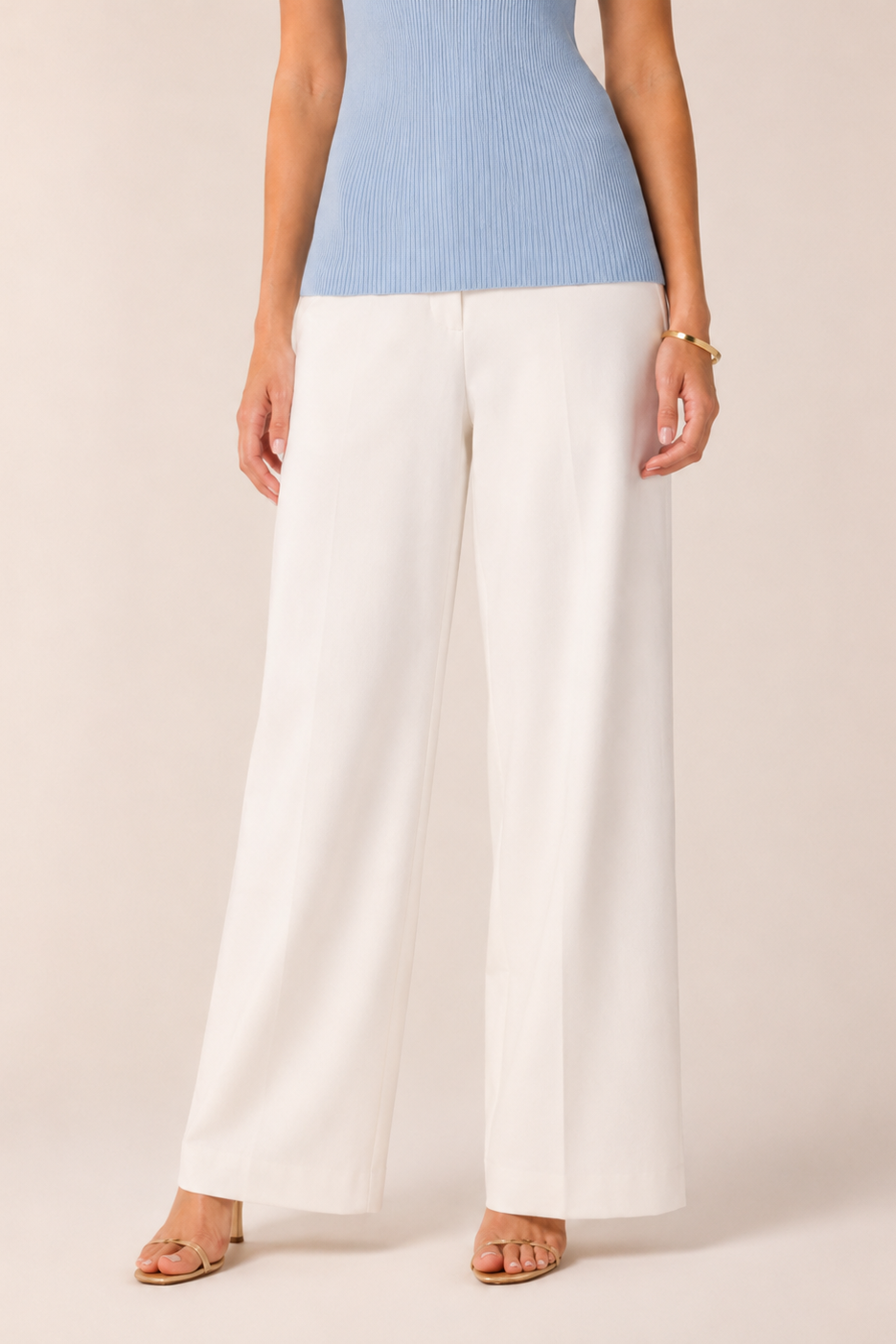 Person wearing a light blue sleeveless top and white wide-leg pants on a beige background