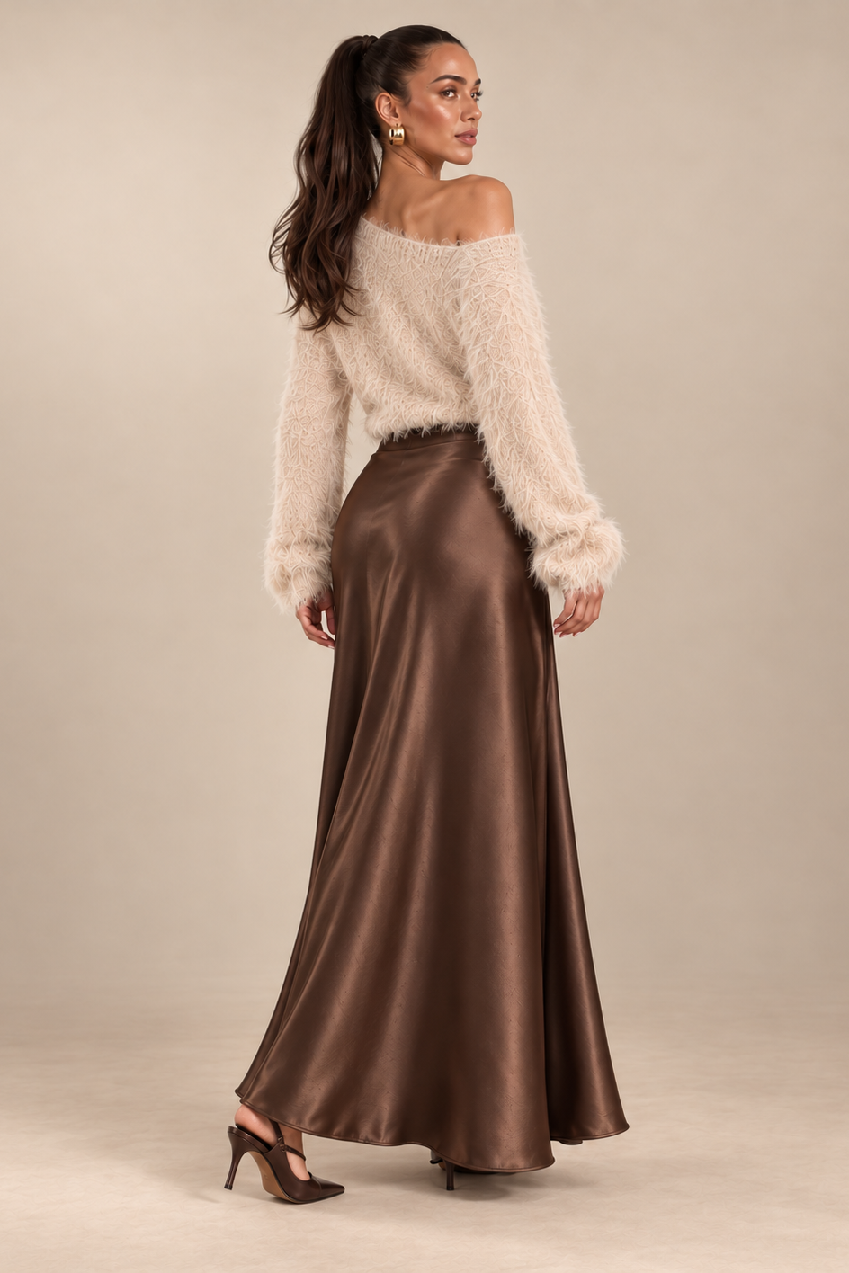 A woman modeling a cream off-the-shoulder fuzzy sweater and a high-waisted, floor-length brown satin skirt against a solid beige studio background.