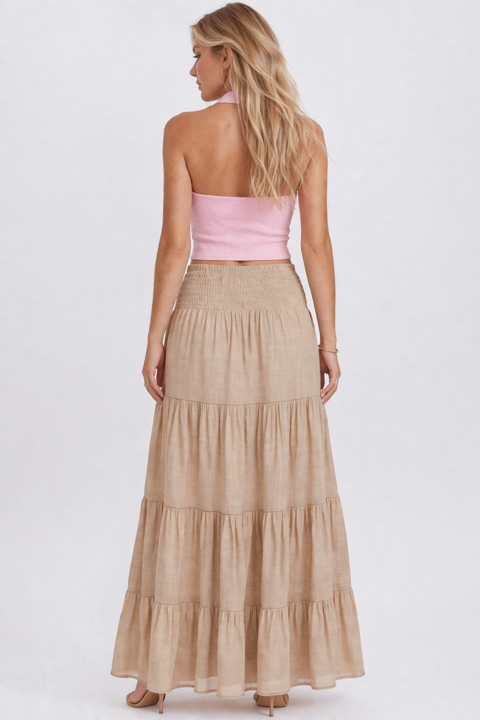 Woman wearing a pink strapless top and beige tiered skirt on a white background