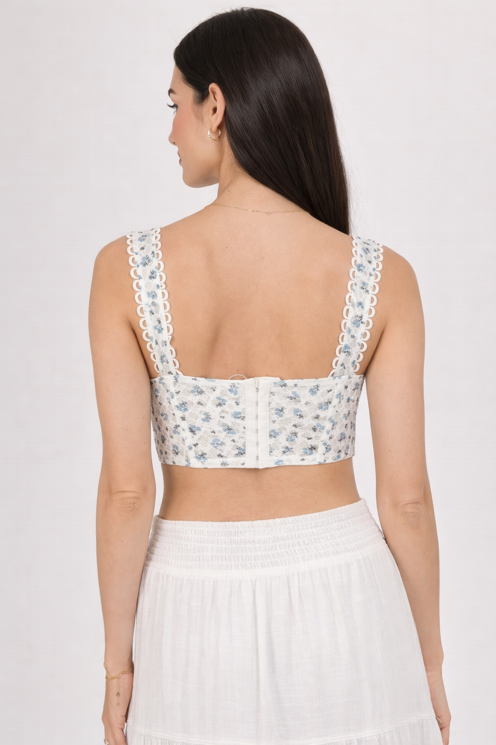 Woman wearing a white floral crop top with lace straps on a plain background