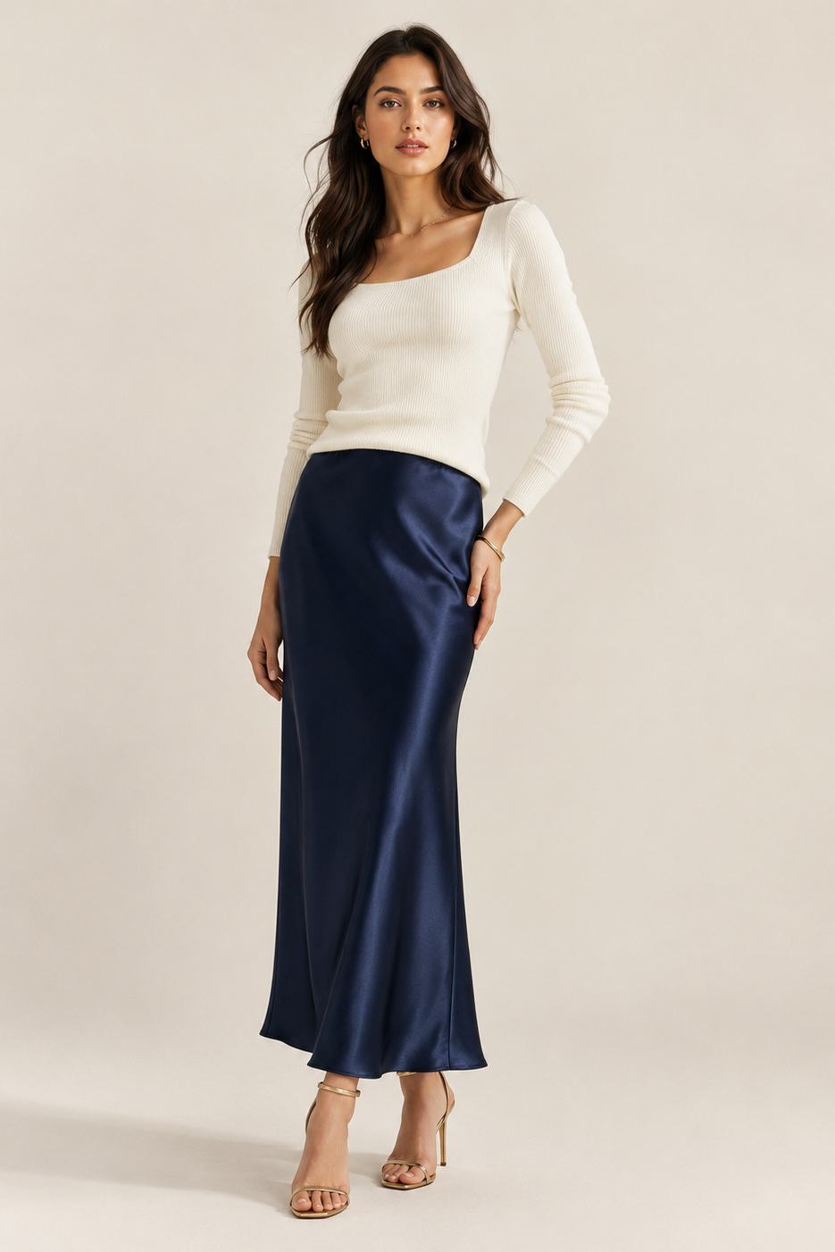 Woman wearing a white top and navy satin skirt on a plain background