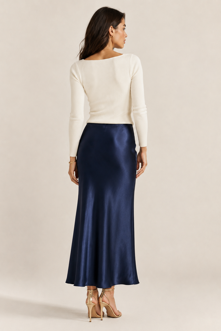 Woman wearing a white top and navy satin skirt on a beige background