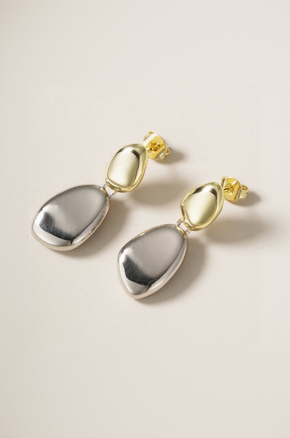 Pair of gold and silver earrings on a beige background