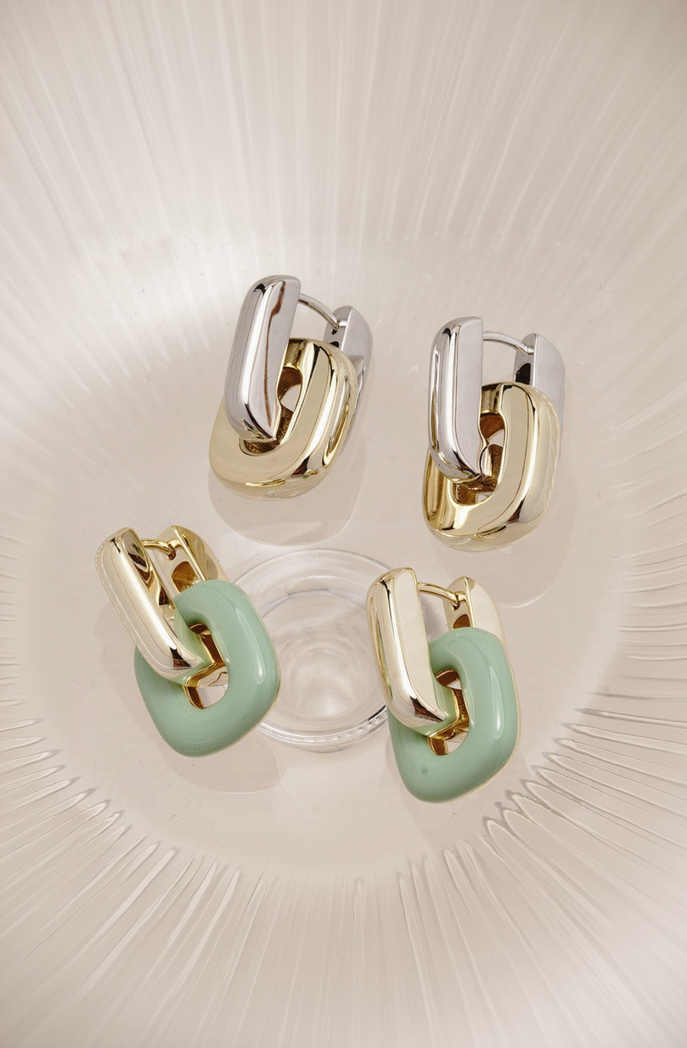 Gold and silver hoop earrings with green accents on a textured surface