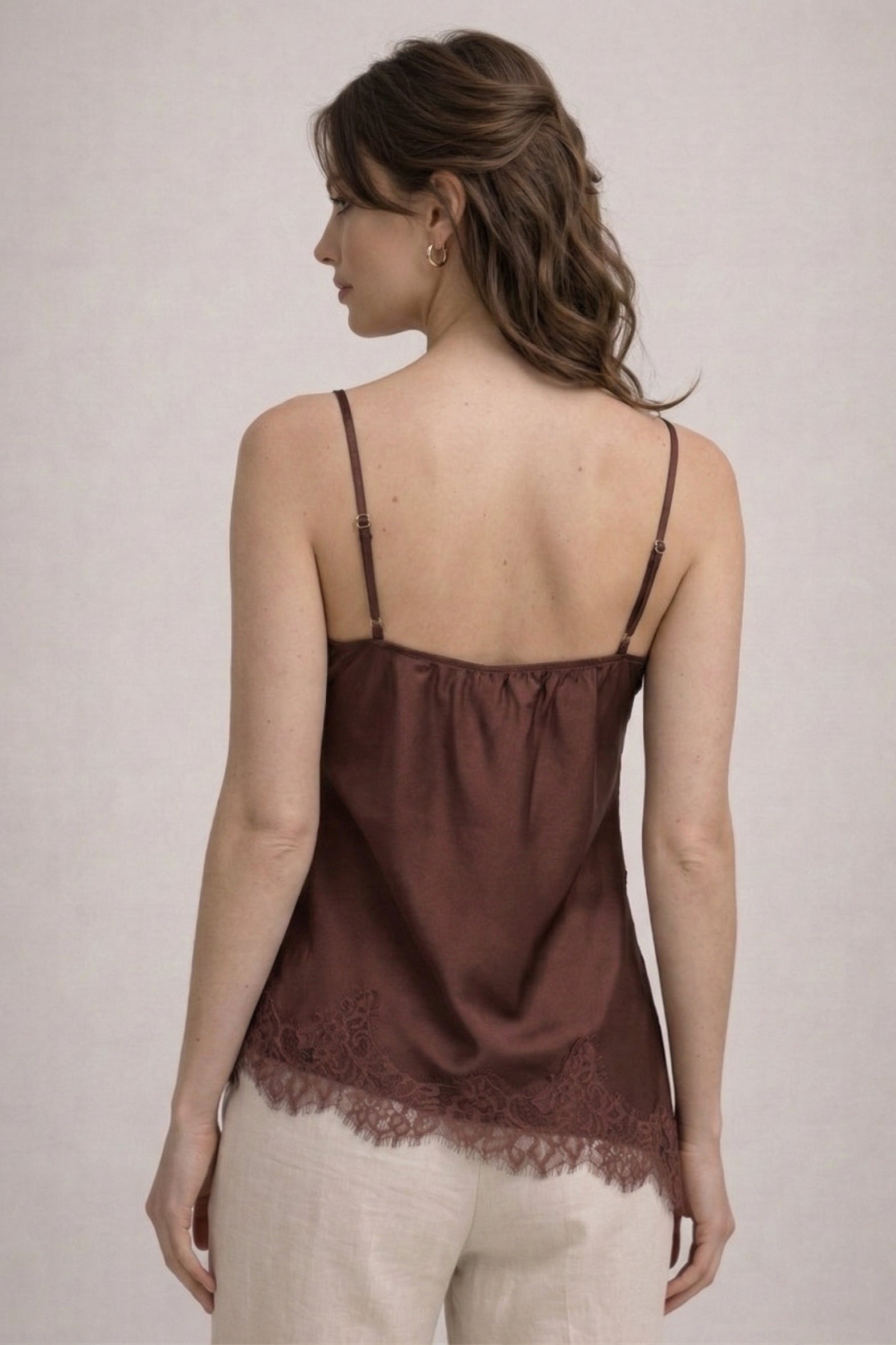 Woman wearing a brown lace-trimmed top against a plain background