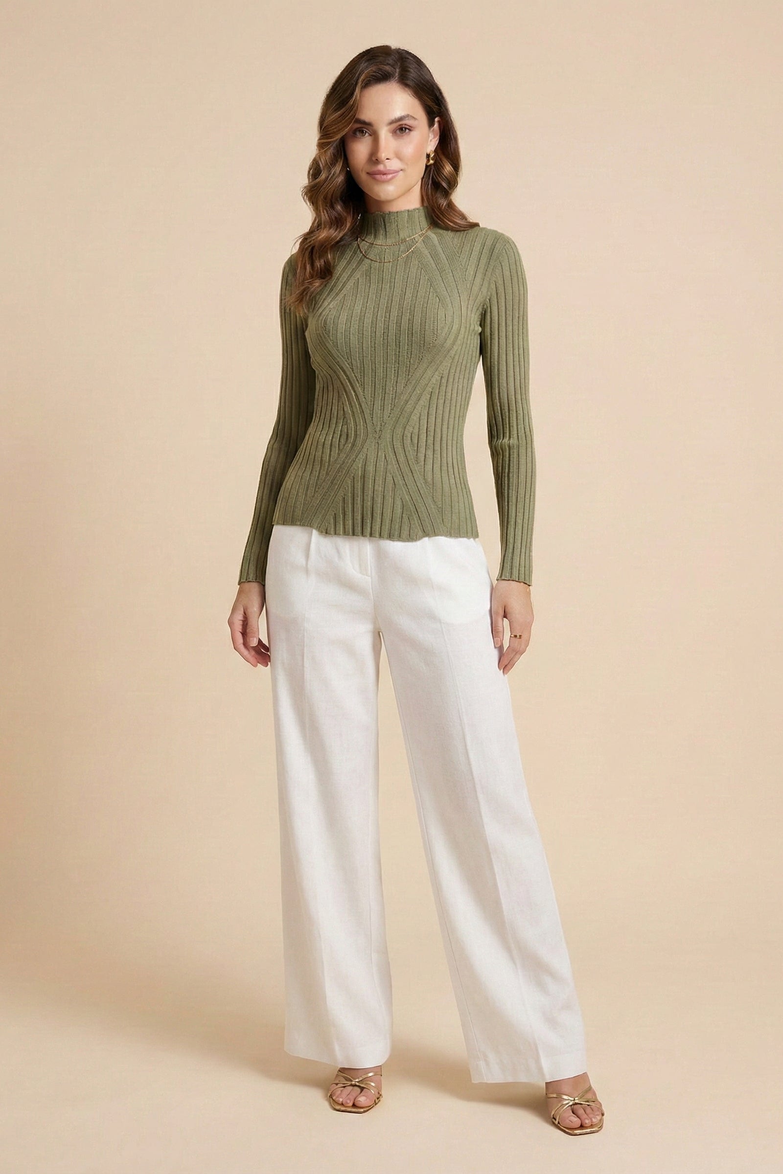 Woman wearing a green ribbed sweater and white pants on a beige background